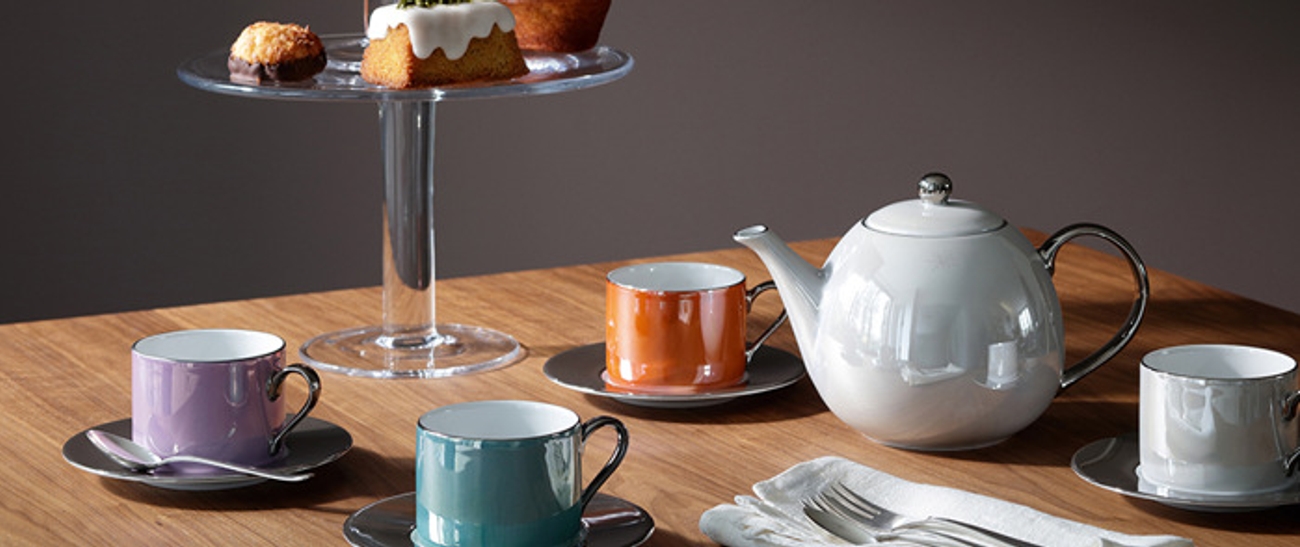 Tekanna i vitt och koppar i olika färger på träbord 