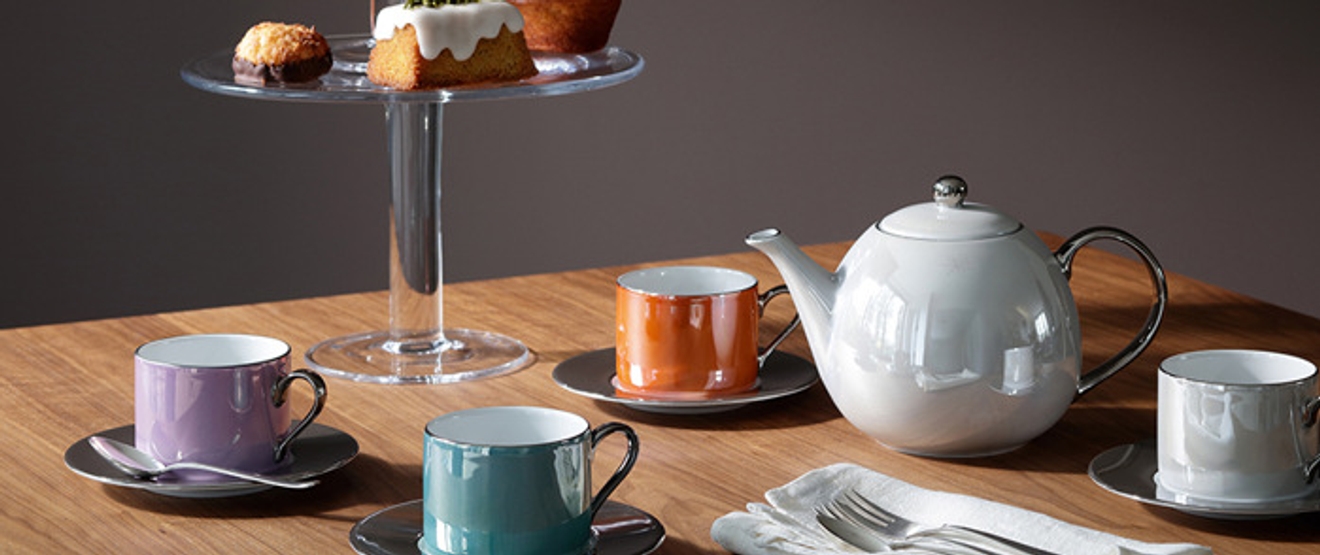 Tekanna i vitt och koppar i olika färger på träbord 