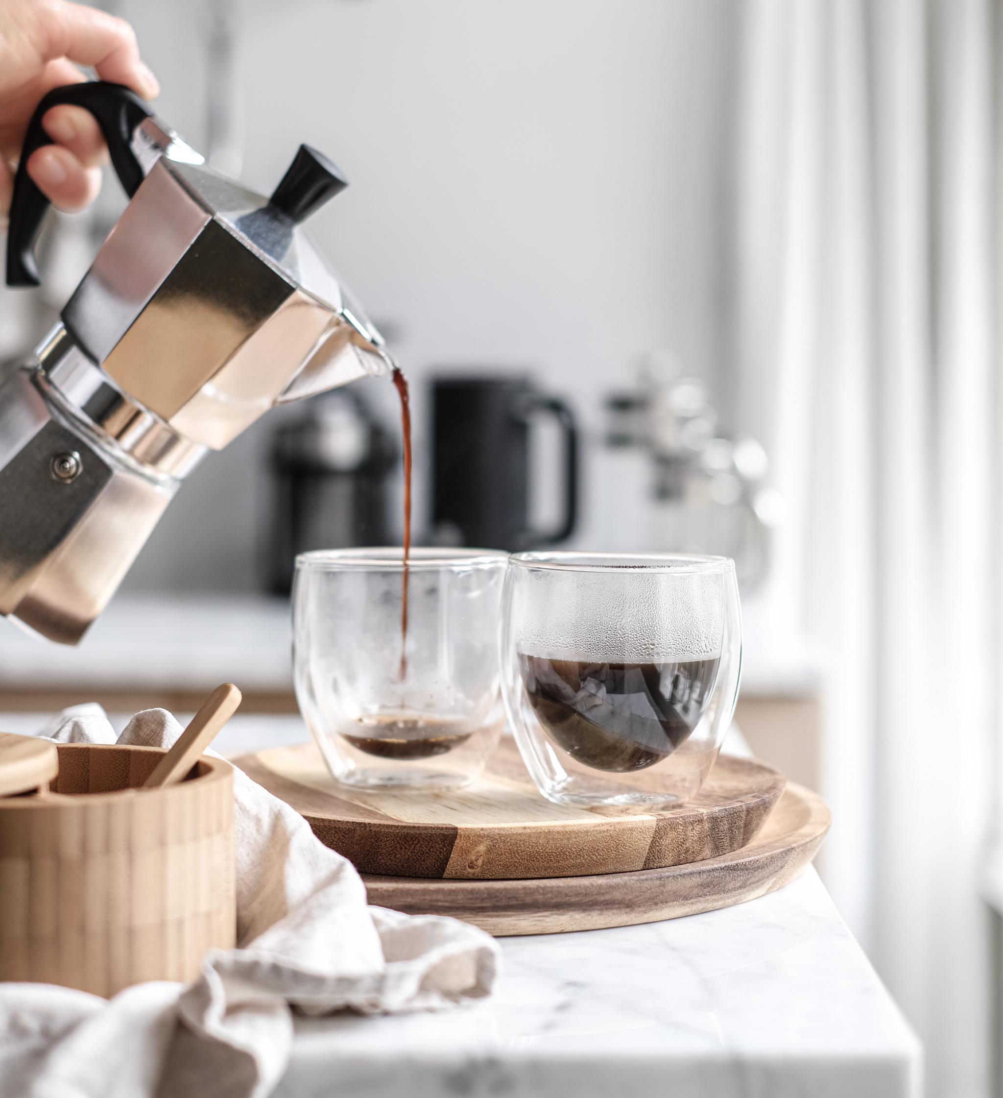 En person heller opp kaffe i to kopper på en kjøkkenbenk
