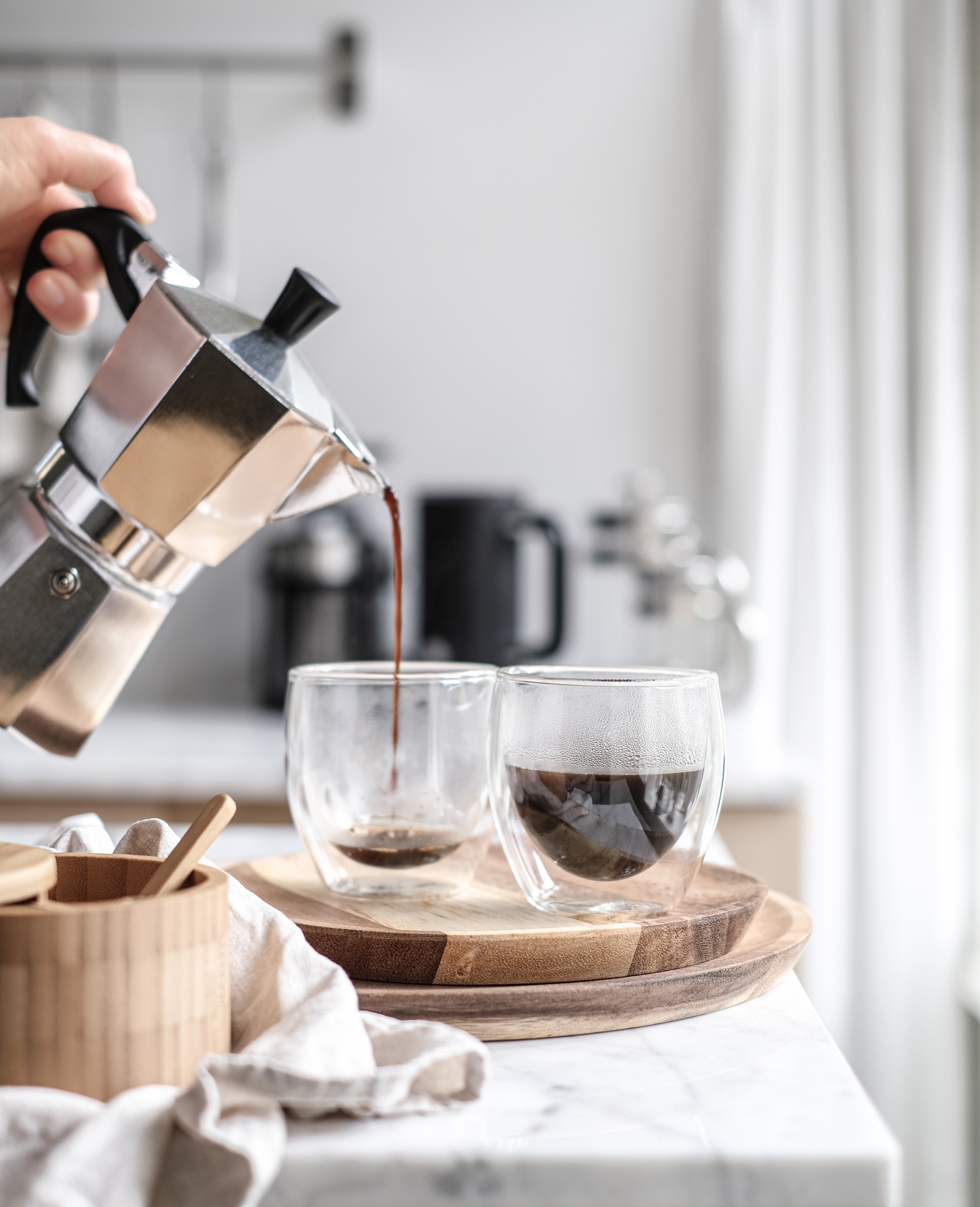 En person heller opp kaffe i to kopper på en kjøkkenbenk