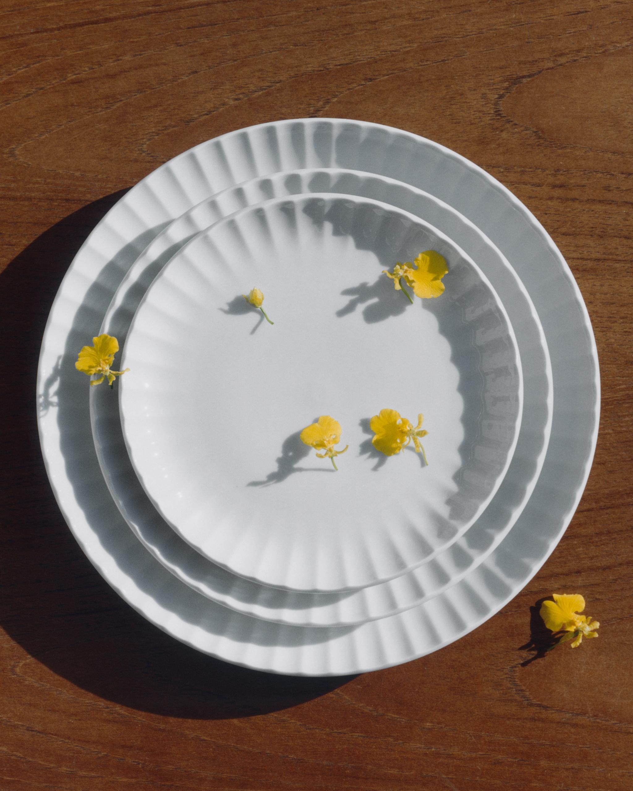 Tre vita, vågiga tallrikar staplade på en träyta med gula blommor.