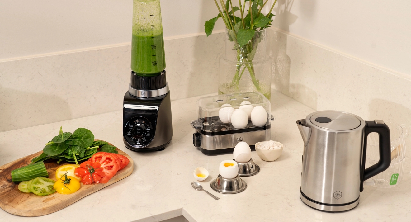 A kitchen counter with a blender, egg cooker, electric kettle, fresh vegetables, and eggs.