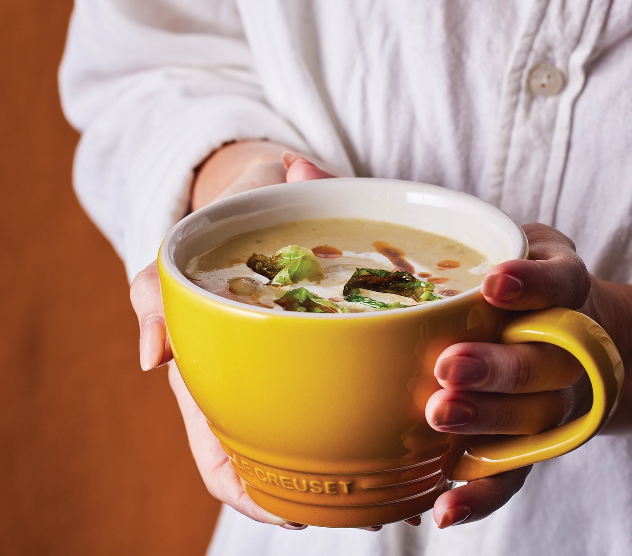 en kvinna håller en gul Le Creuset-mugg med soppa