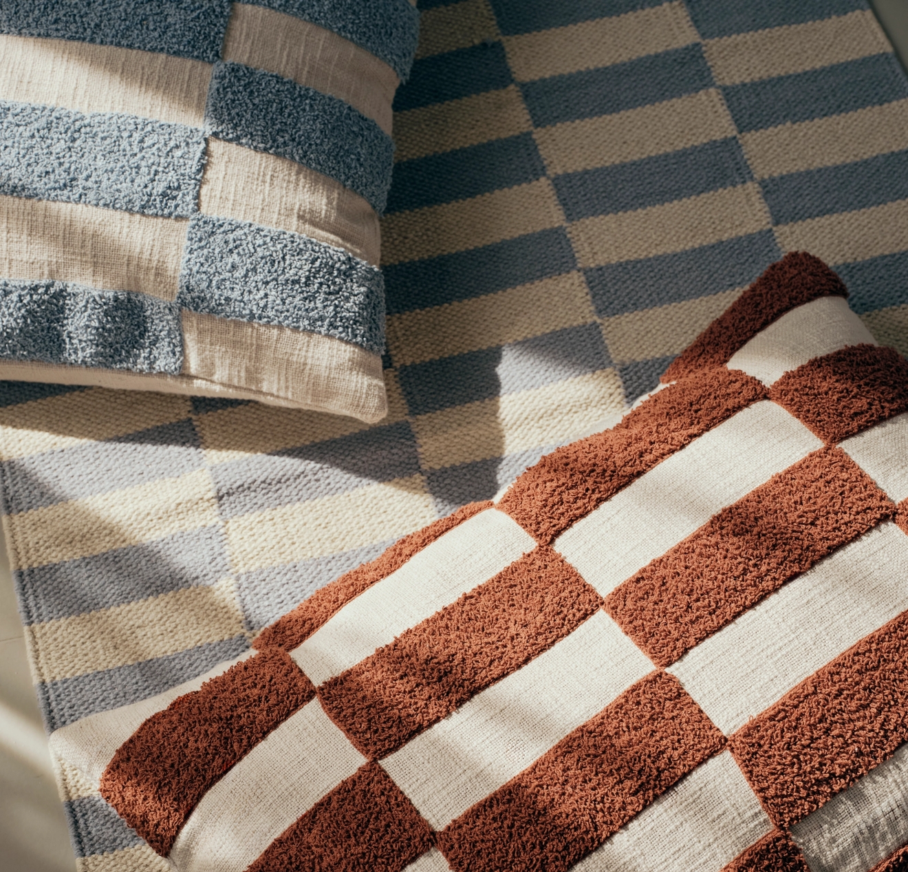 Randiga frottéhanddukar i rostbrunt, beige och blågrått på en mönstrad textil.