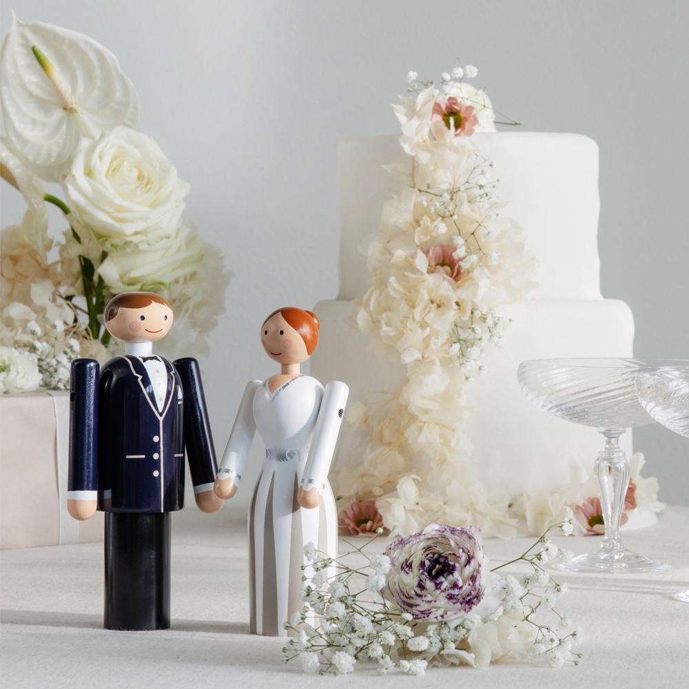 Bröllopstårta med vita blommor, glas och två stiliserade brudparfigurer som dekoration.