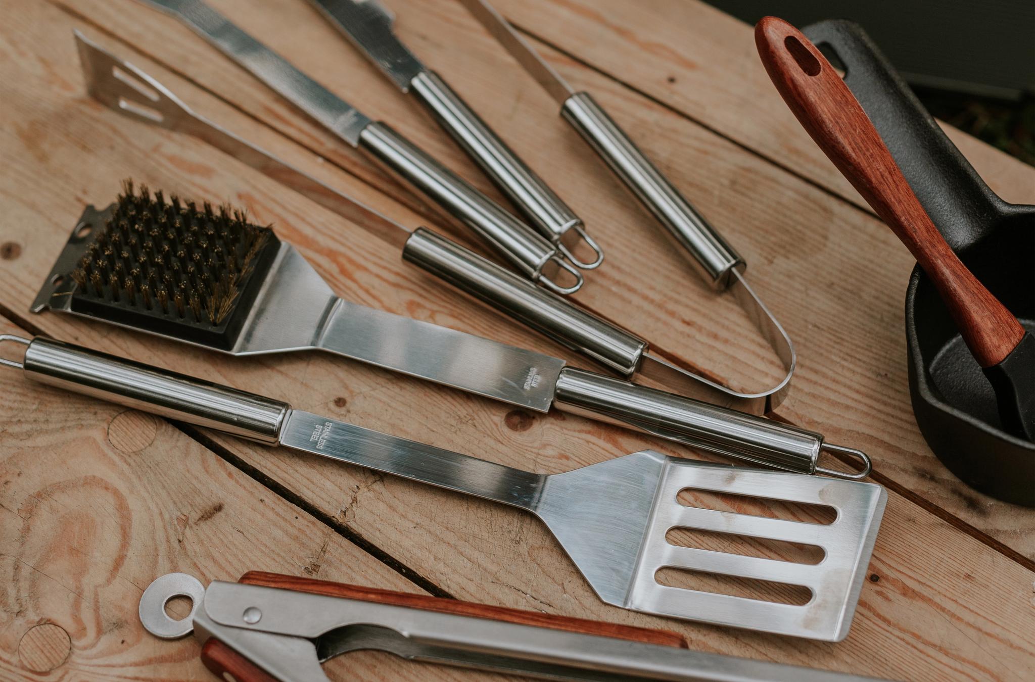 Närbild av grillverktyg i rostfritt stål på en träyta.