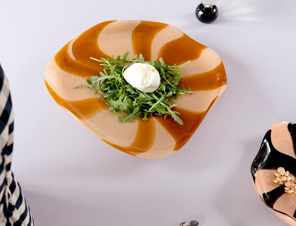 Tyylikkäällä aaltomaisella lautasella tarjoiltu rucolasalaatti ja burrata-juusto kattauksessa.
