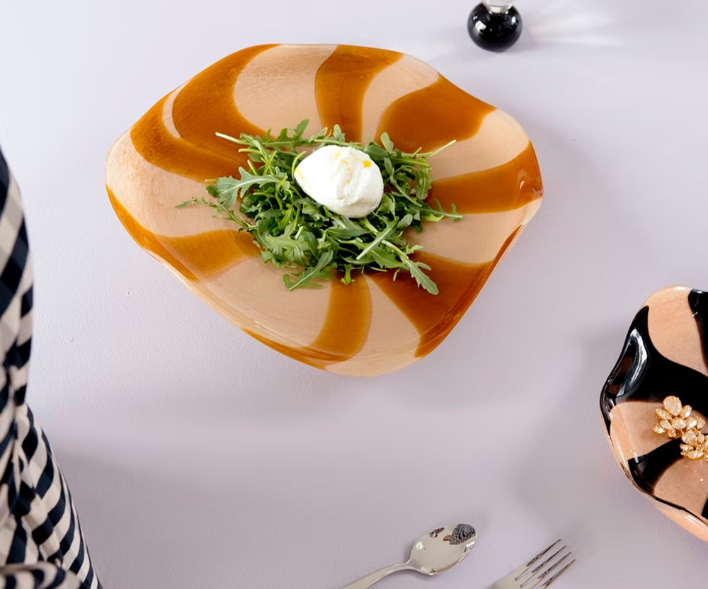Tyylikkäällä aaltomaisella lautasella tarjoiltu rucolasalaatti ja burrata-juusto kattauksessa.