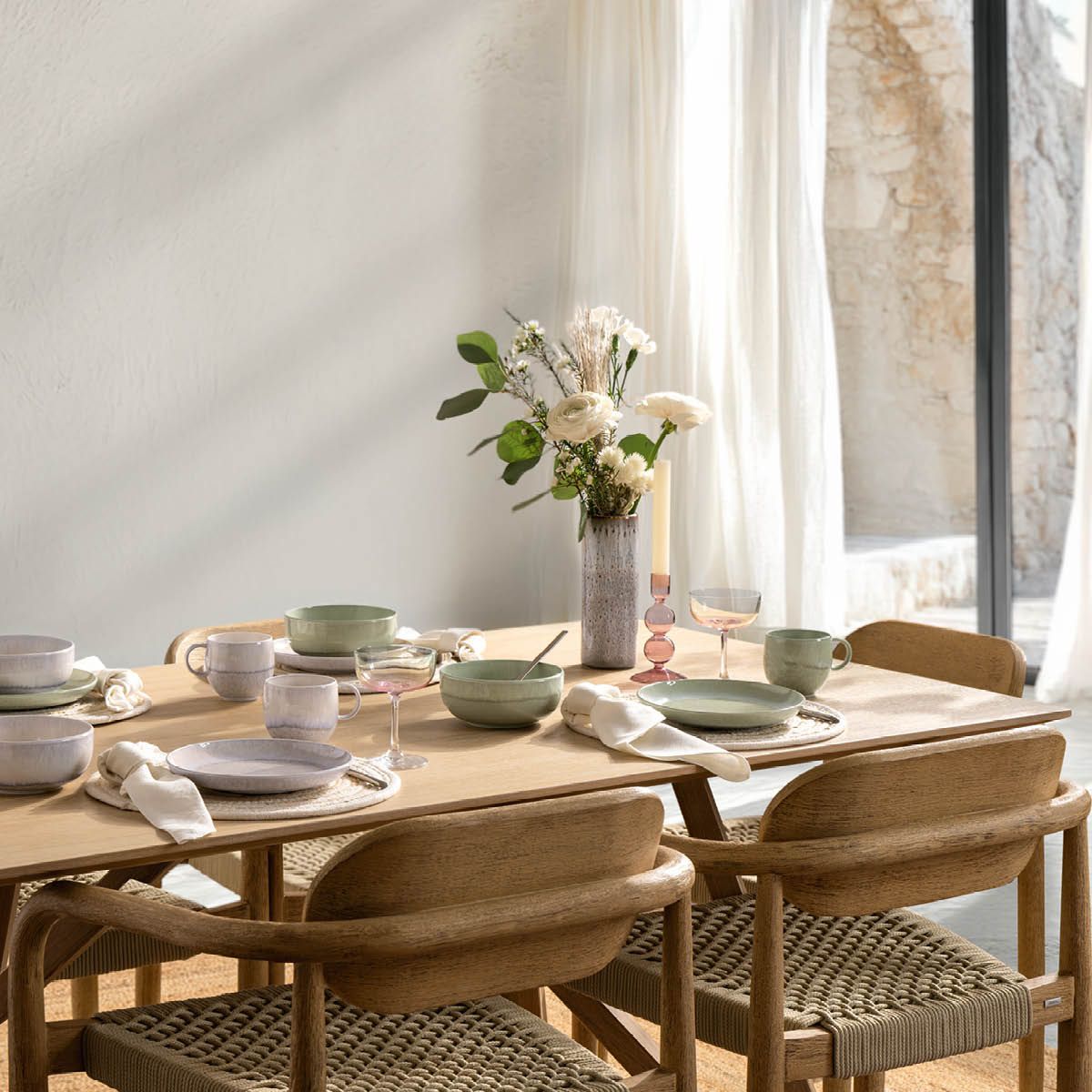 ett matbord med tallrikar, skålar, glas och en vas med blommor på det.