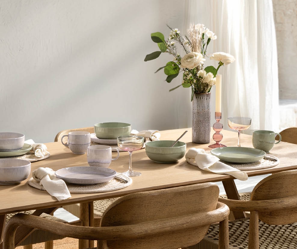 Ljust och modernt matbord dukat med keramik, glas och blommor i en skandinavisk inredning.