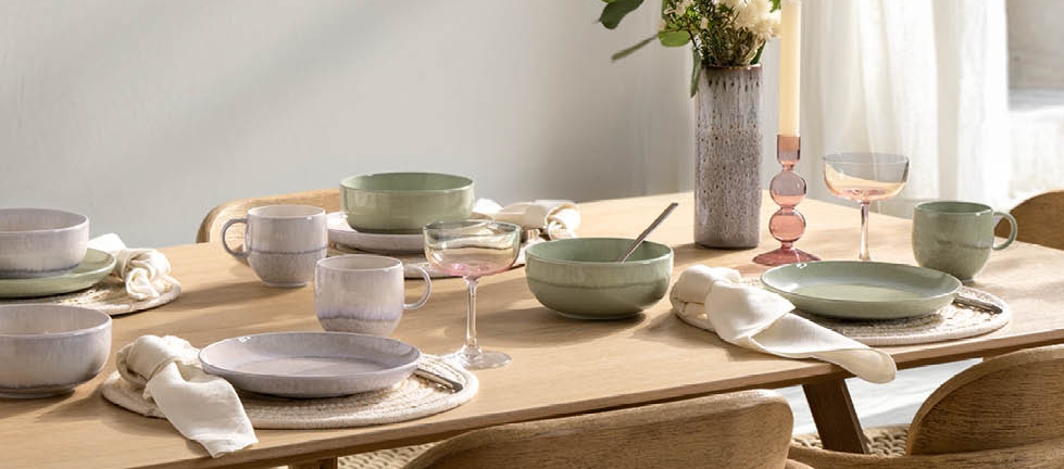 Ljust och modernt matbord dukat med keramik, glas och blommor i en skandinavisk inredning.