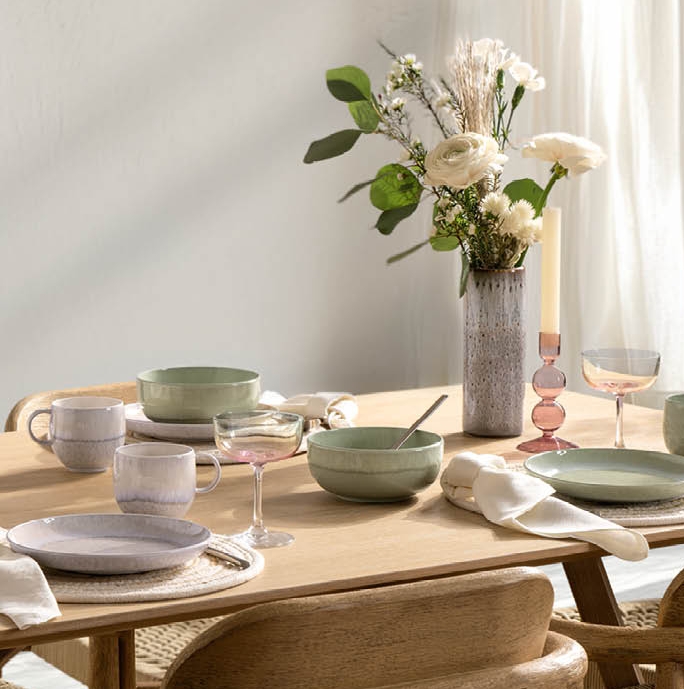 ett matbord med tallrikar, skålar, glas och en vas med blommor på det.