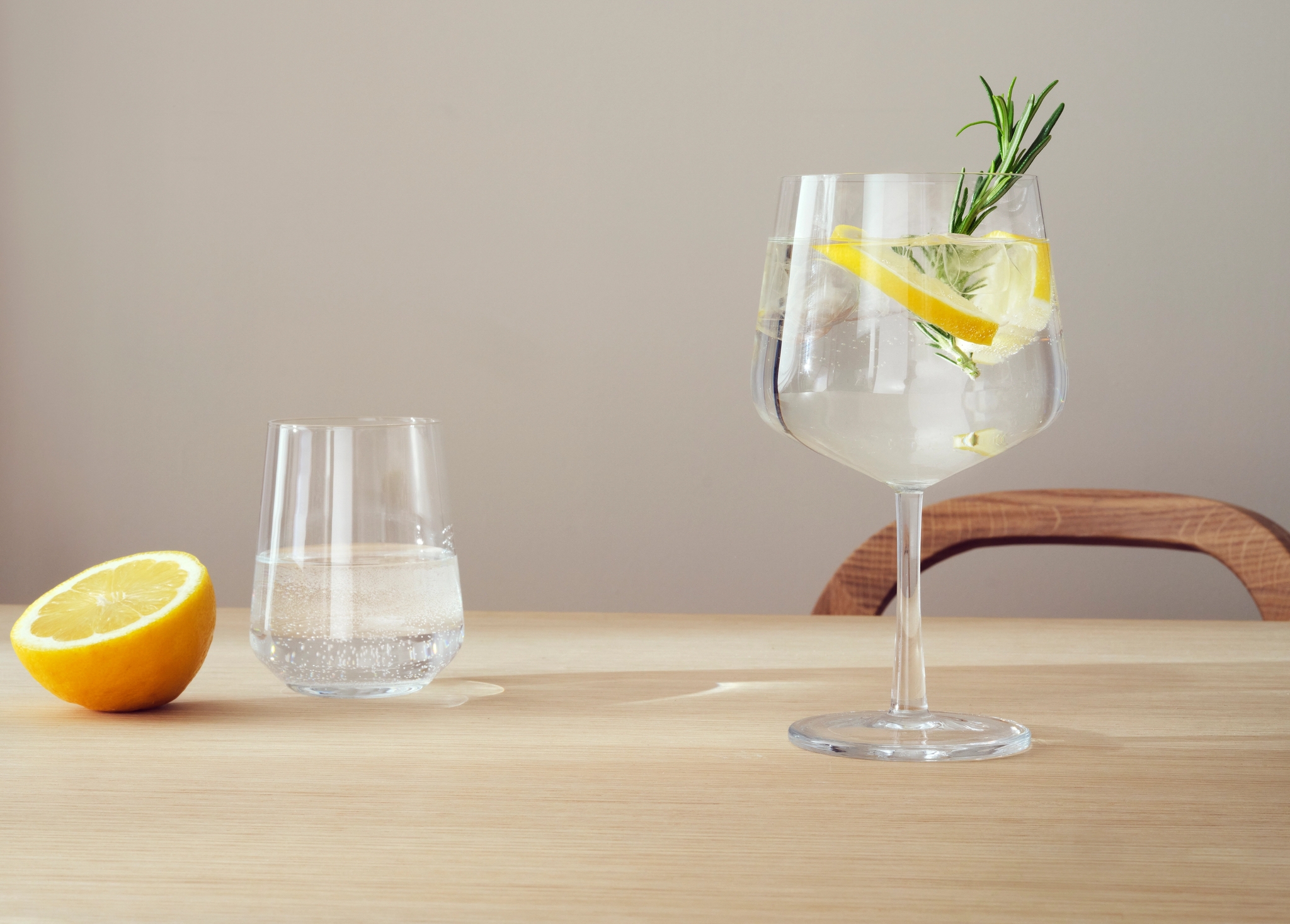 Vaalealla puupöydällä on puolitettu sitruuna, lasillinen kivennäisvettä ja varrellinen vesilasi, koristeltuna sitruunalla ja yrteillä.