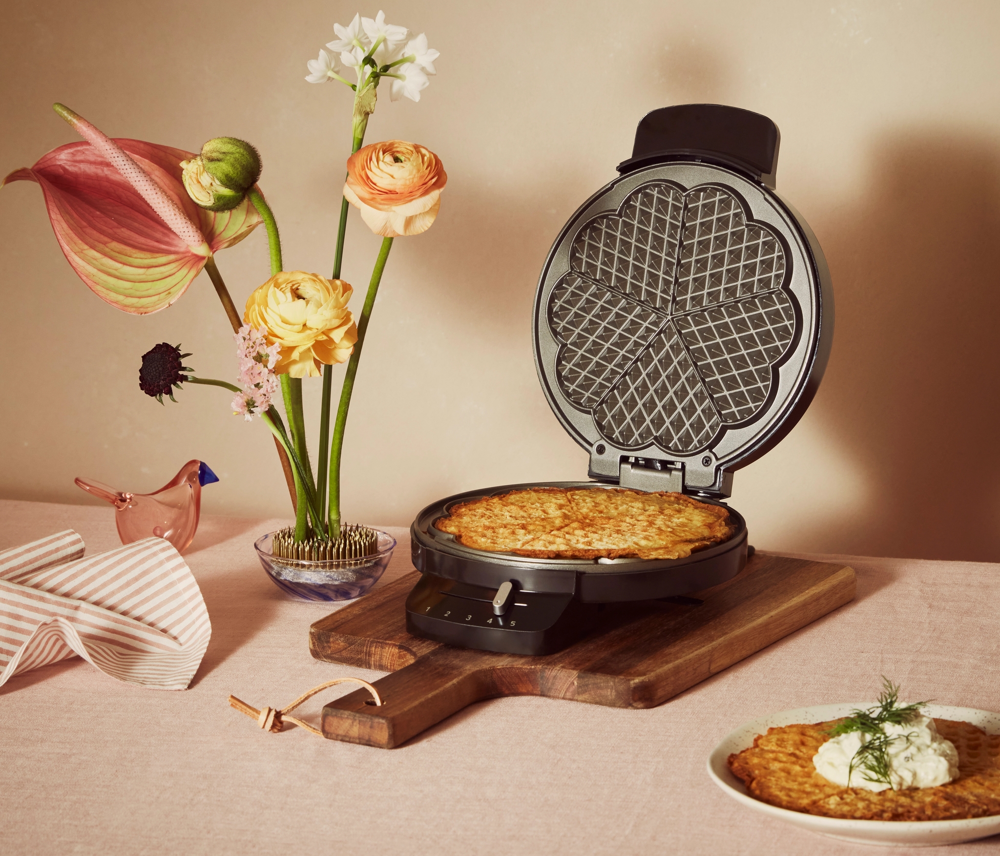 Enkelt svart våffeljärn med en våffla i på ett bord med blommor