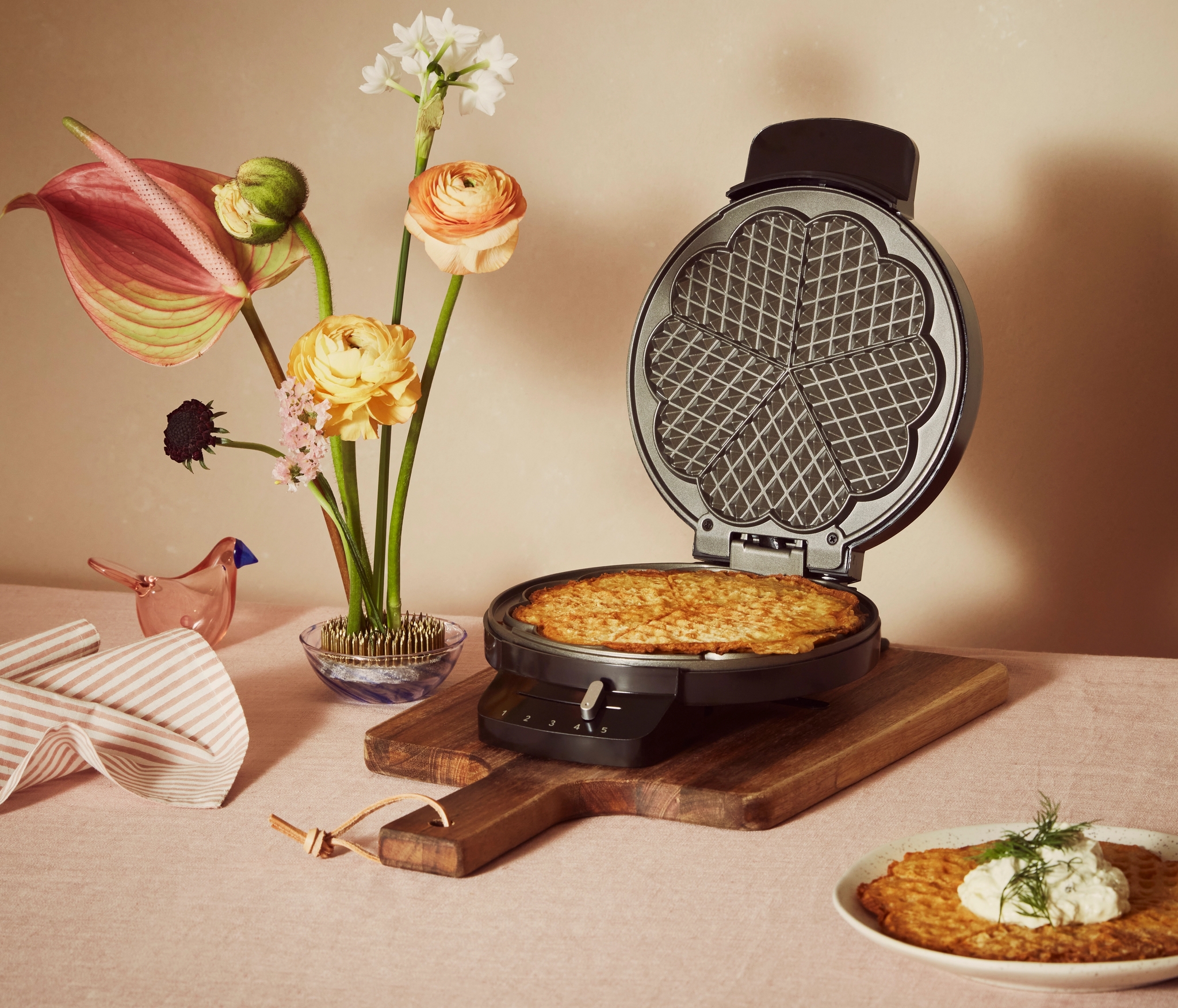 Enkelt svart våffeljärn med en våffla i på ett bord med blommor