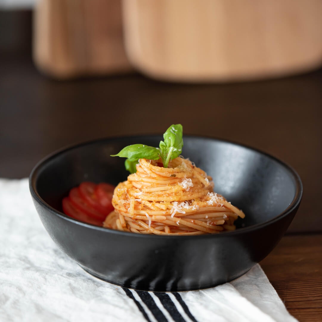 Pastatallrik i svart med spagetti och tomatsås toppat med parmesan och basilika