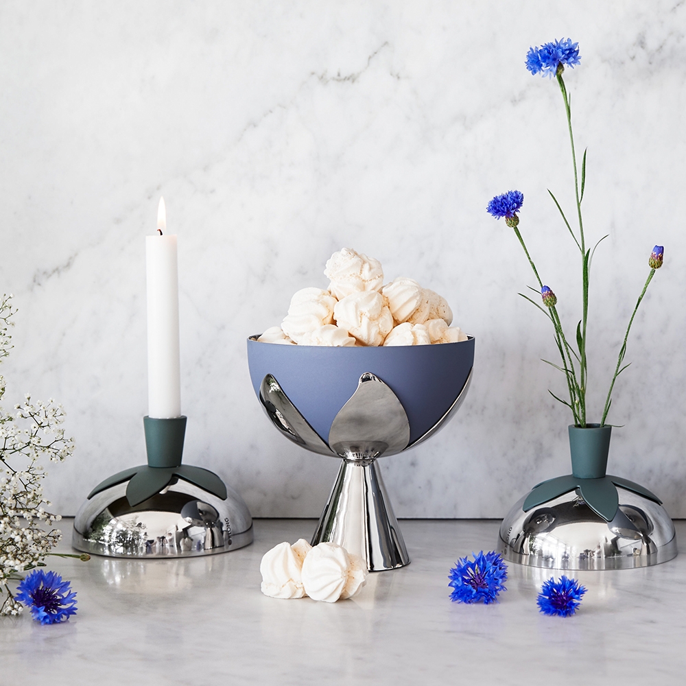 Modern silver, blue, and green-accented tabletop set: a bowl with meringues, a lit candle, and blue cornflowers in a vase, on marble.