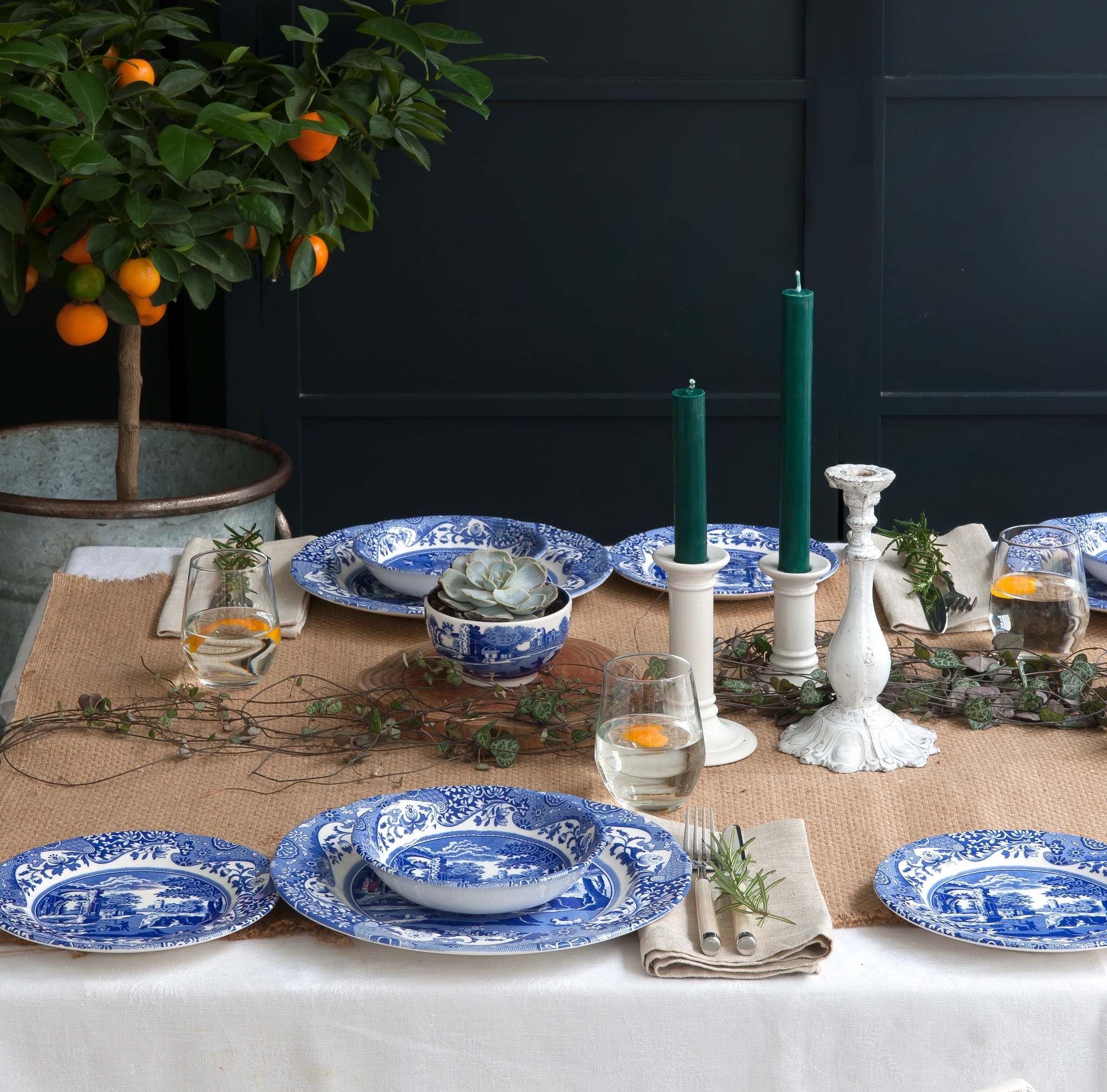 sinivalkoiset lautaset katetulla pöydällä kynttilälyhtyjen ja viherkasvien kera