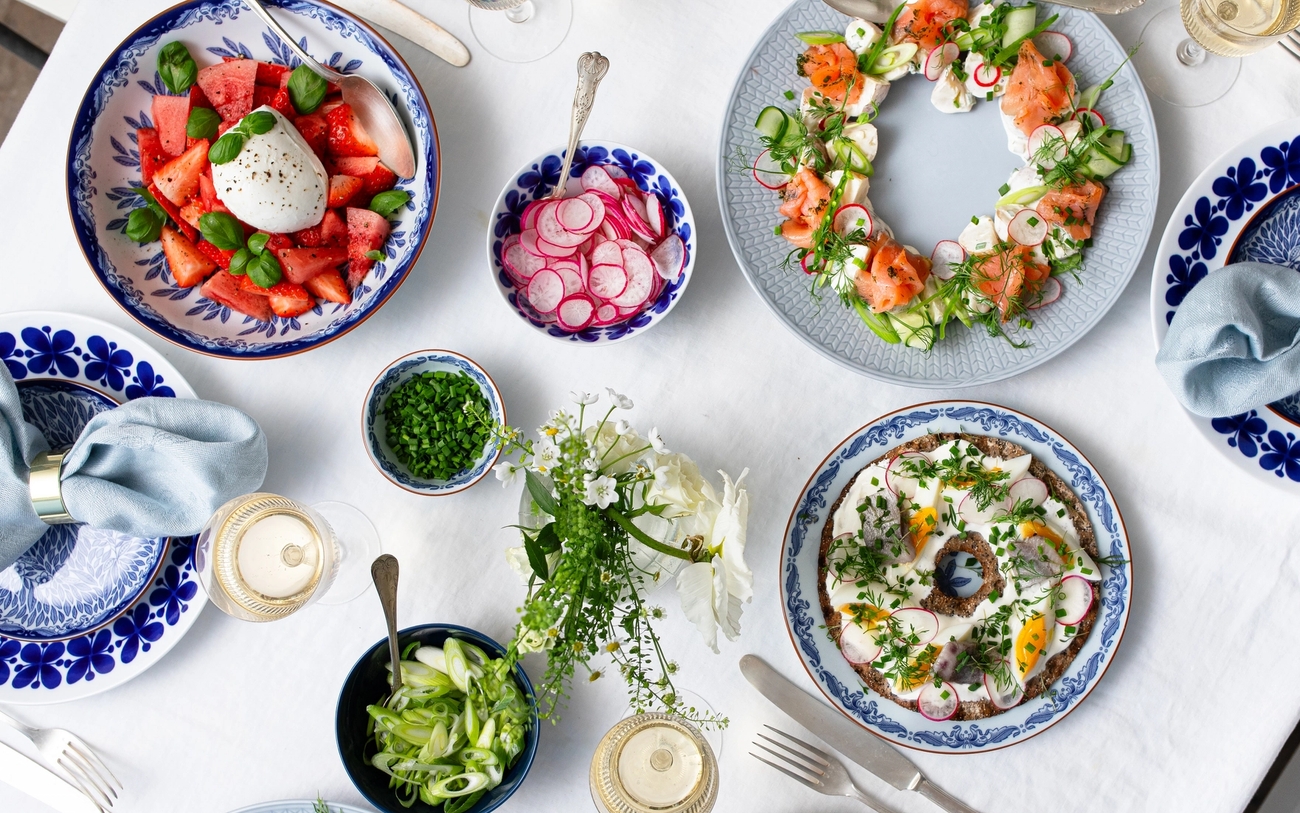 Vacker sommarbuffé med burratasallad, lax, sill och rädisor uppdukat på blåvita tallrikar