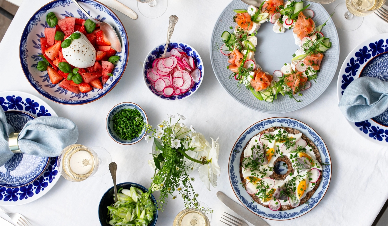 Vacker sommarbuffé med burratasallad, lax, sill och rädisor uppdukat på blåvita tallrikar