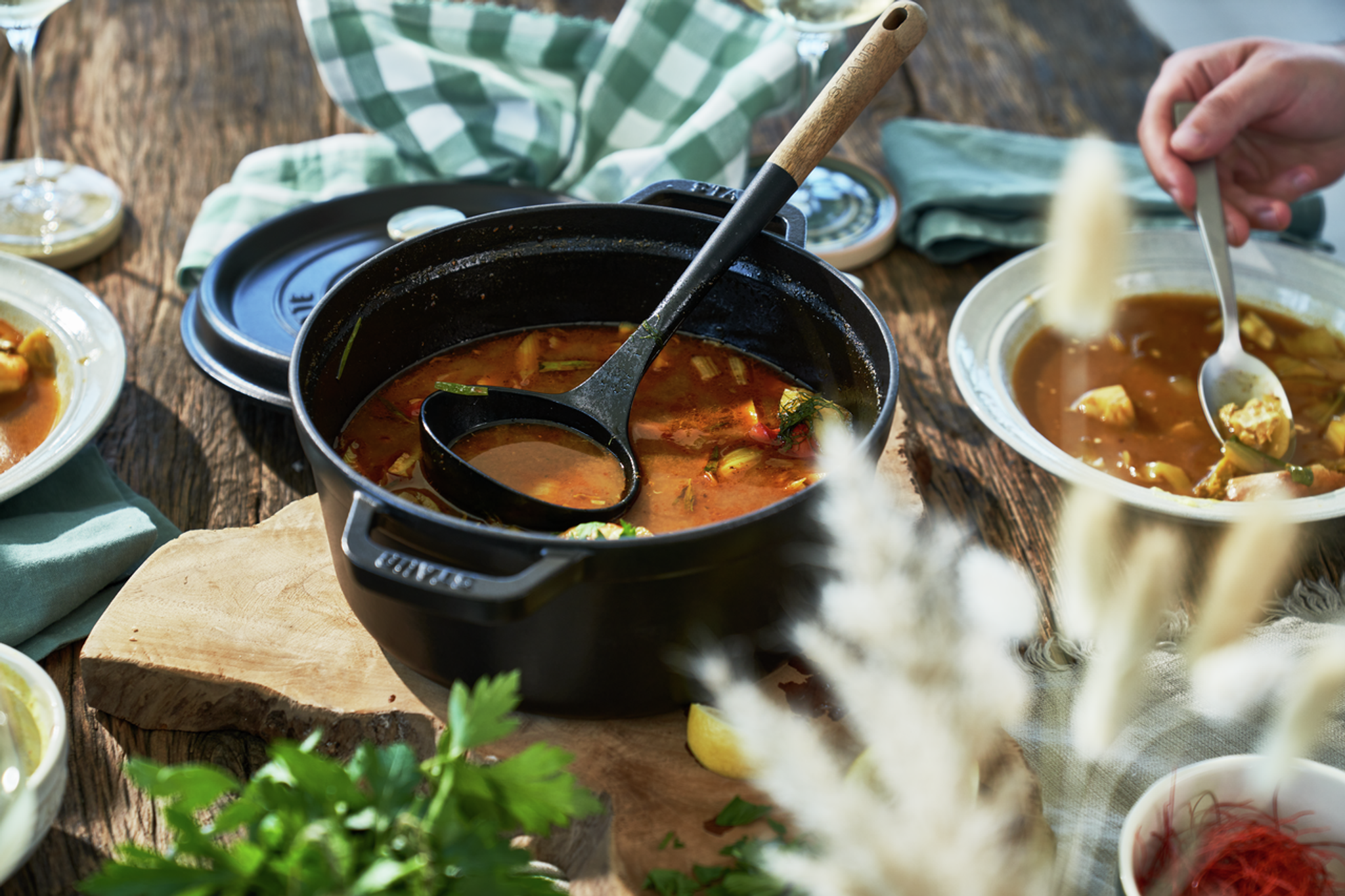 Valurautainen pata kauhoineen ja kulho tarjoiltuna maalaismaisella ulkopöydällä.