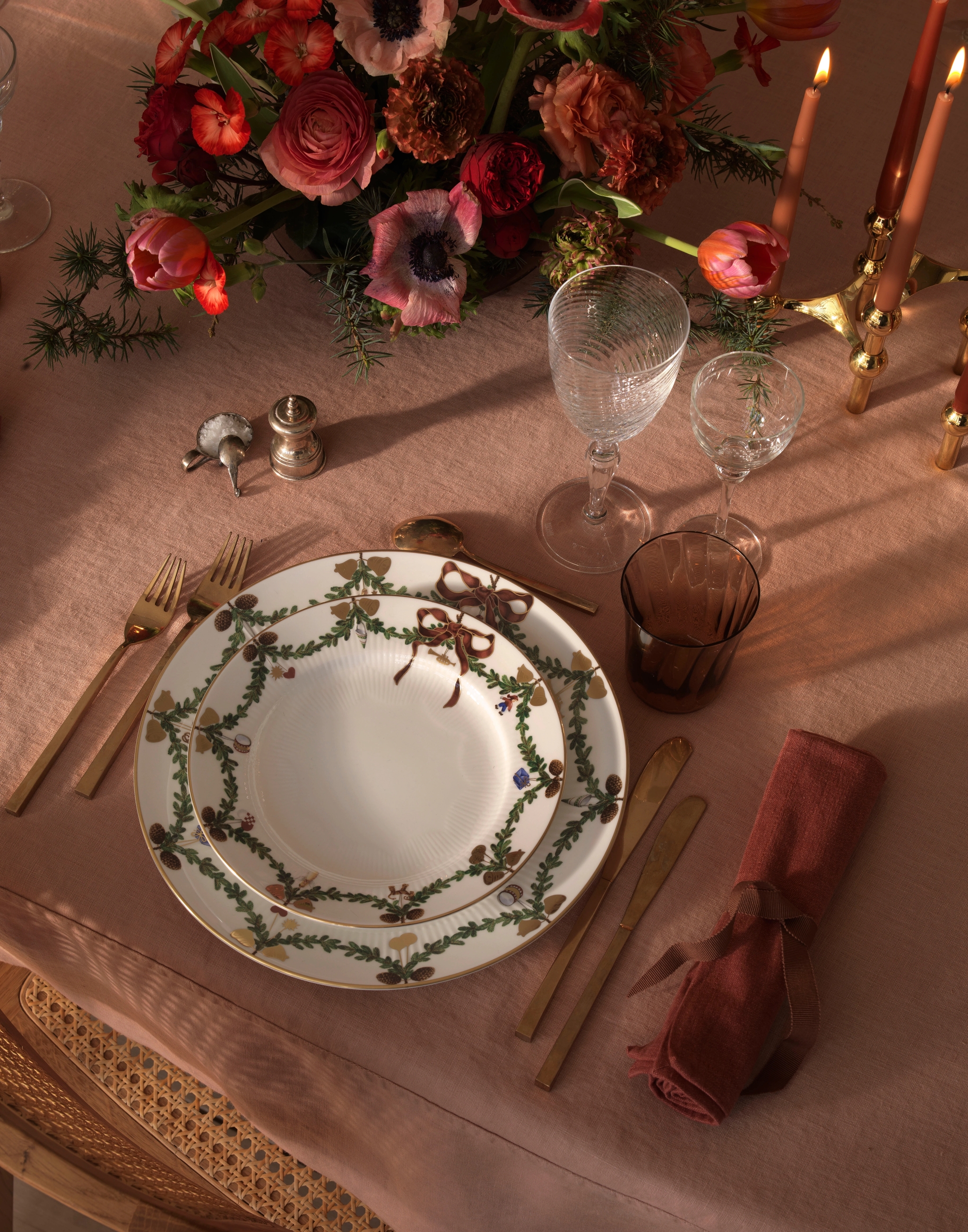 Ett dukat bord för en middagsbjudning med julporslin, ljus och blommor.