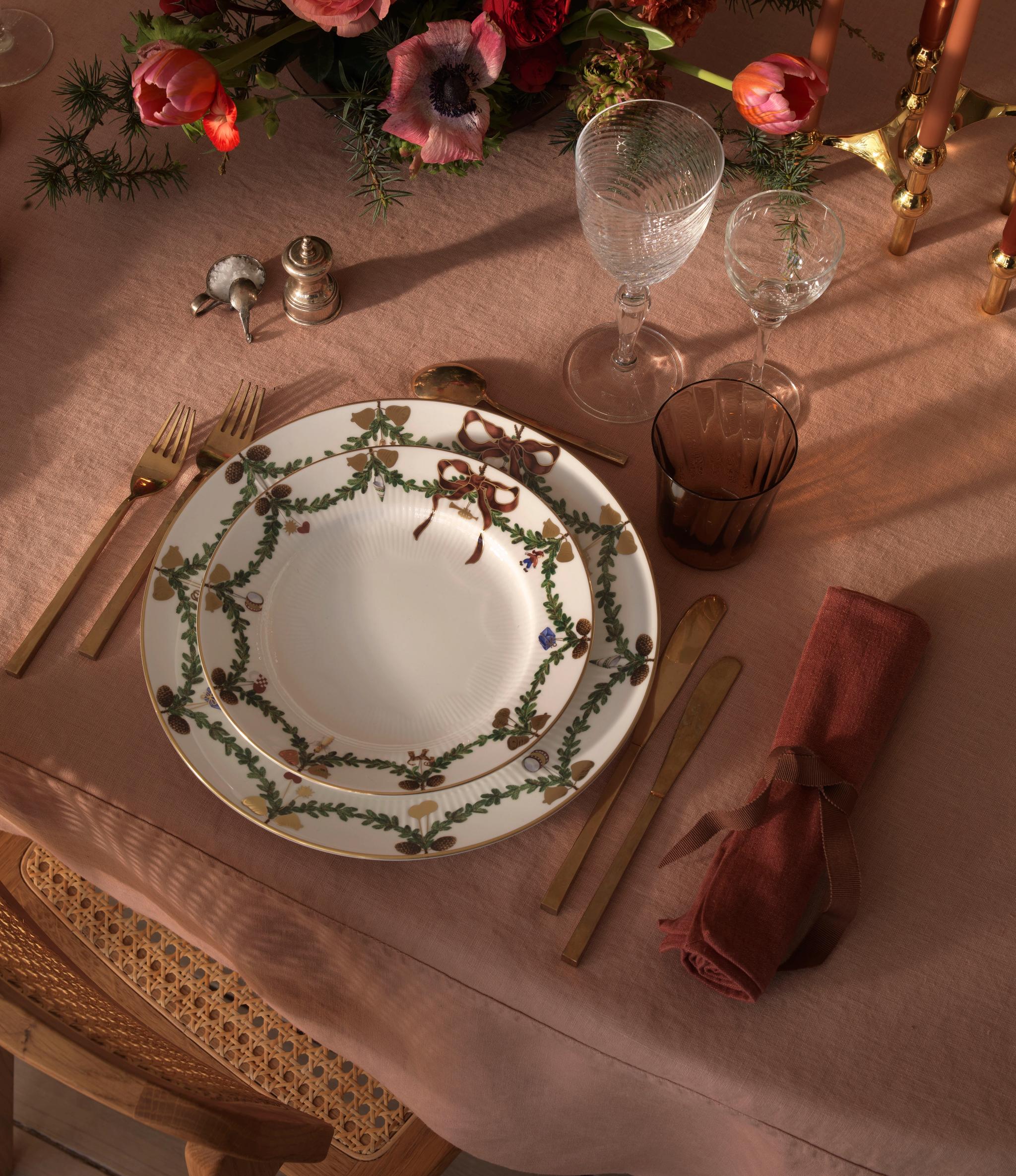Ett dukat bord för en middagsbjudning med julporslin, ljus och blommor.