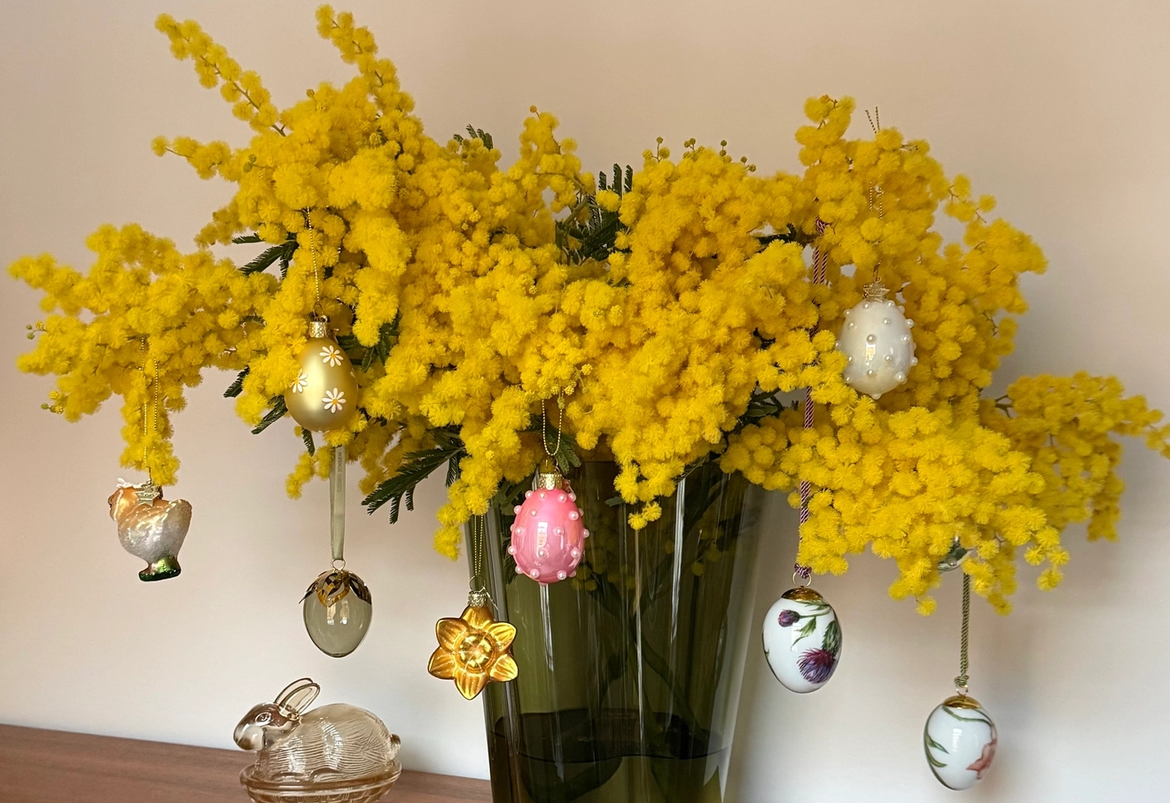 Värikäs kimppu keltaisia mimosankukkia, koristeltu roikkuvilla pääsiäismuna- ja kukkakoristeilla
