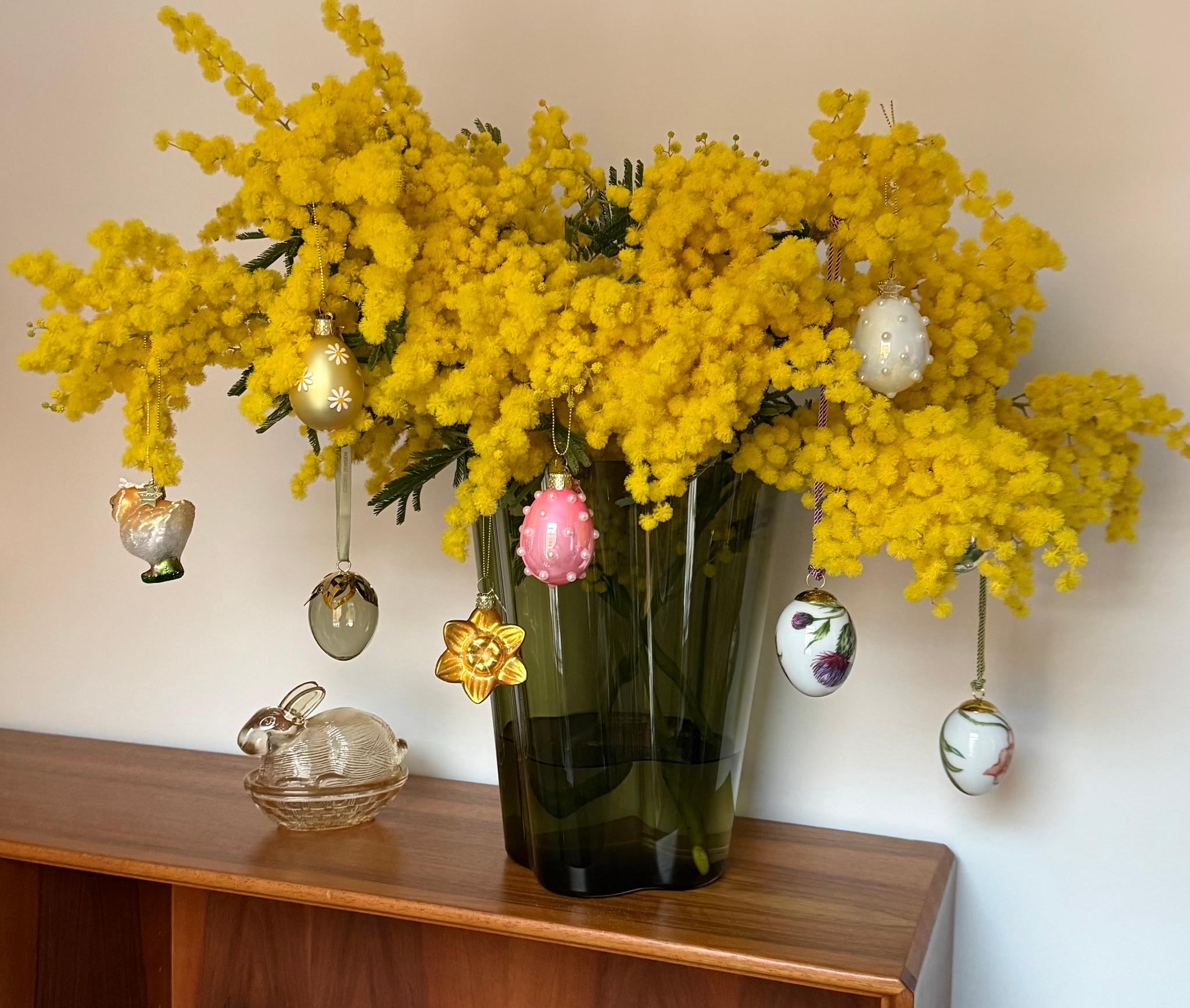 Värikäs kimppu keltaisia mimosankukkia, koristeltu roikkuvilla pääsiäismuna- ja kukkakoristeilla