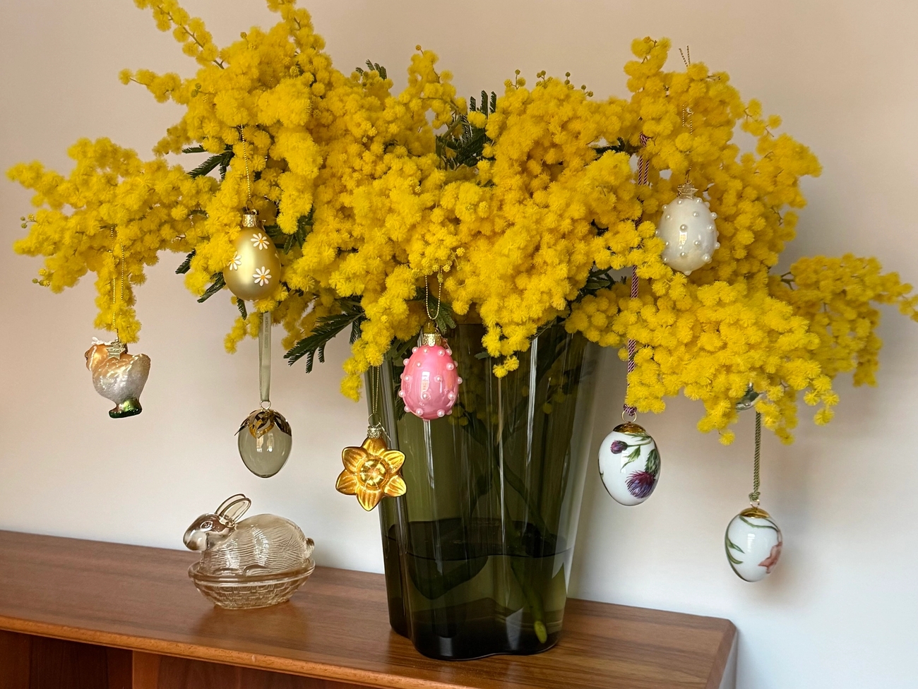 Värikäs kimppu keltaisia mimosankukkia, koristeltu roikkuvilla pääsiäismuna- ja kukkakoristeilla