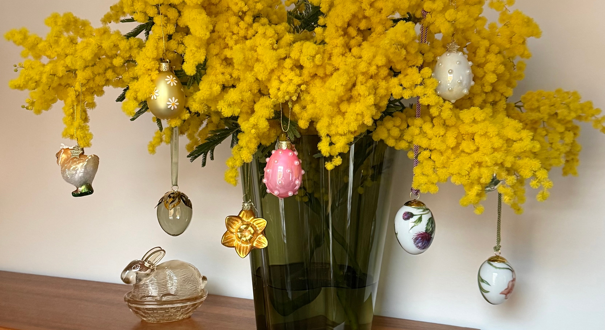 Gule mimosablomster dekorert med hengende påskeeggpynt.