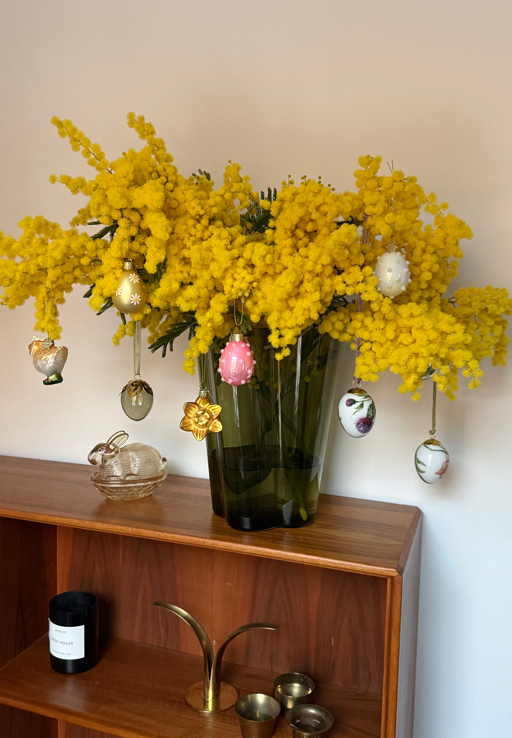 Värikäs kimppu keltaisia mimosankukkia, koristeltu roikkuvilla pääsiäismuna- ja kukkakoristeilla