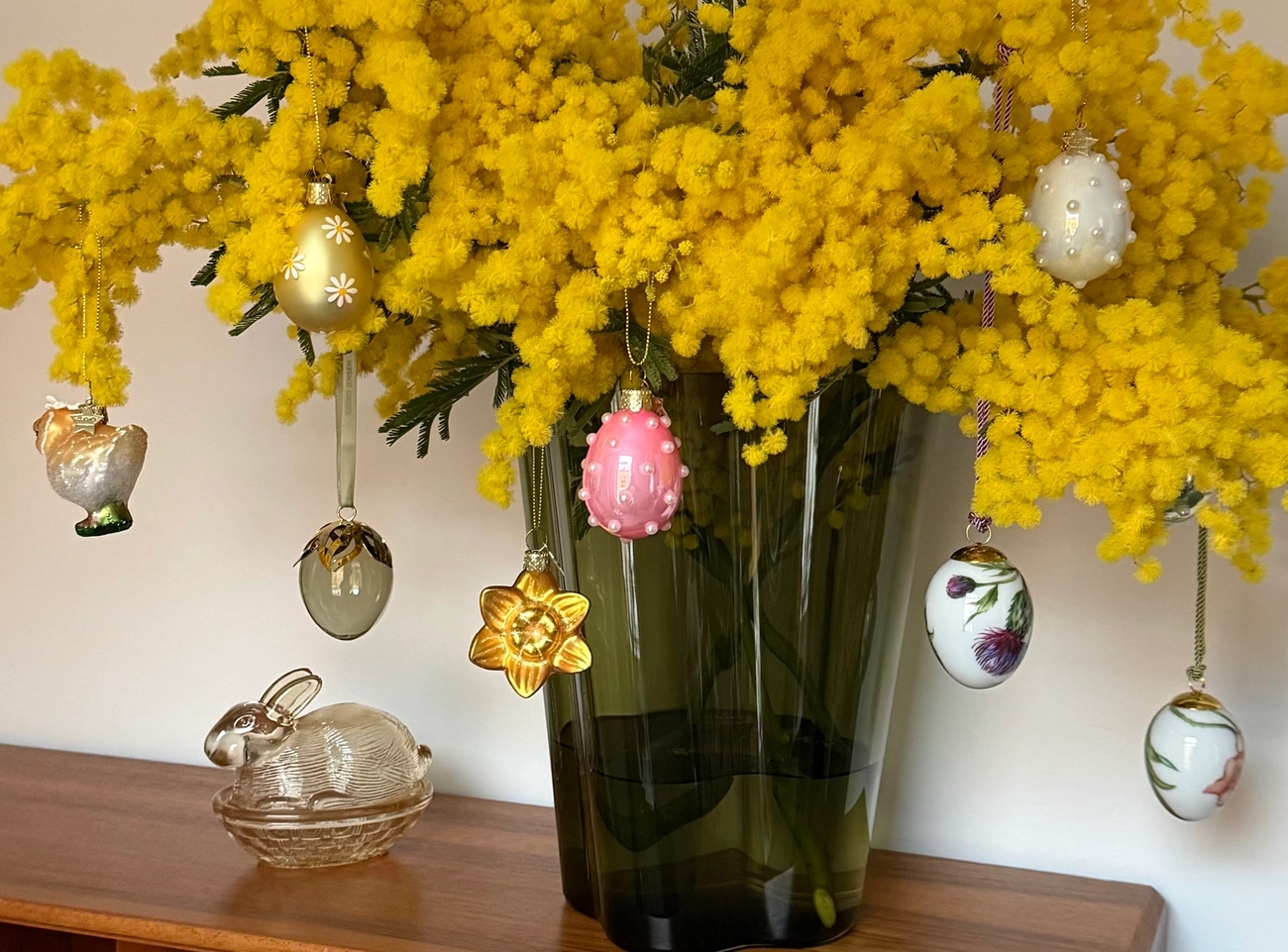 Gule mimosablomster dekorert med hengende påskeeggpynt.