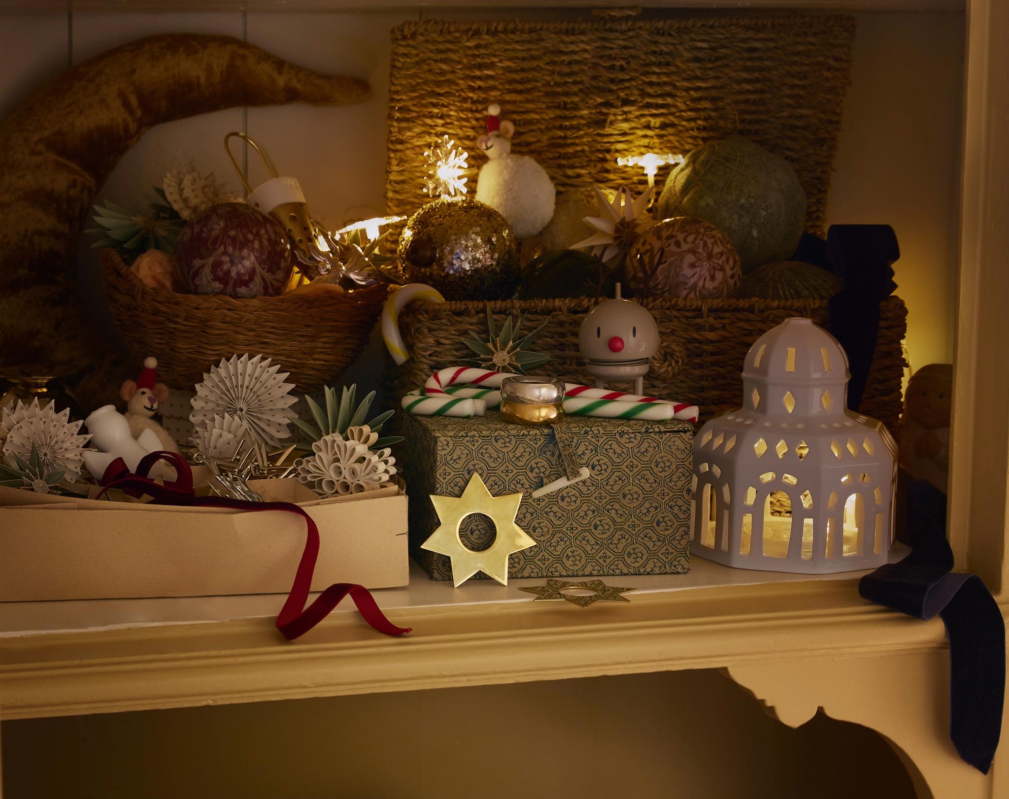 Vitriinikaappi täynnä jouluisia koristeita – hehkuvia tähtivaloja, kuusenkoristeita, lahjoja ja pieniä figuureja – luoden lämpimän ja kodikkaan tunnelman.