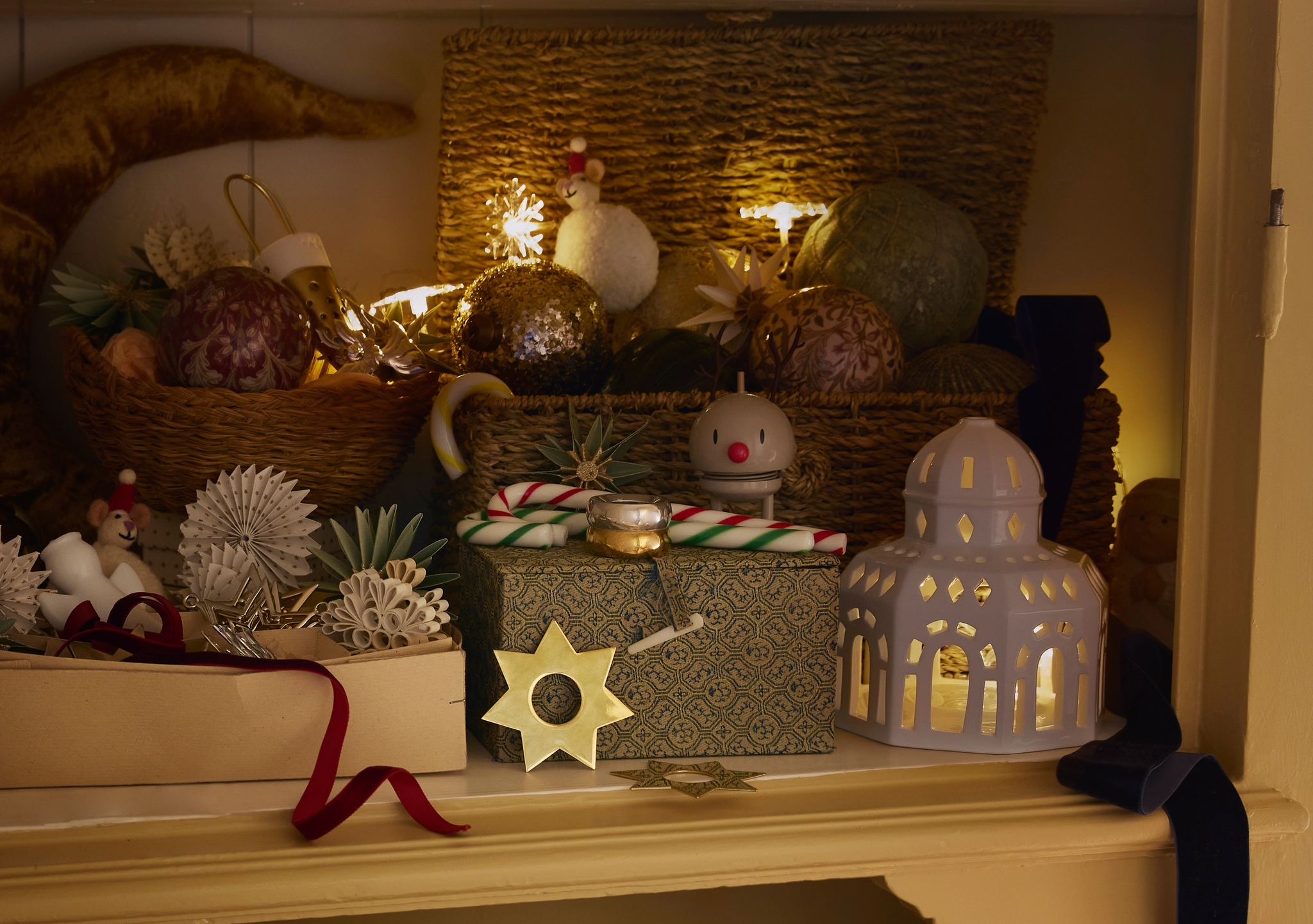 Ett festligt skåp fyllt med stjärnljus, ornament, presenter och tomtar arrangerade i korgar, vilket skapar en mysig juldekoration.