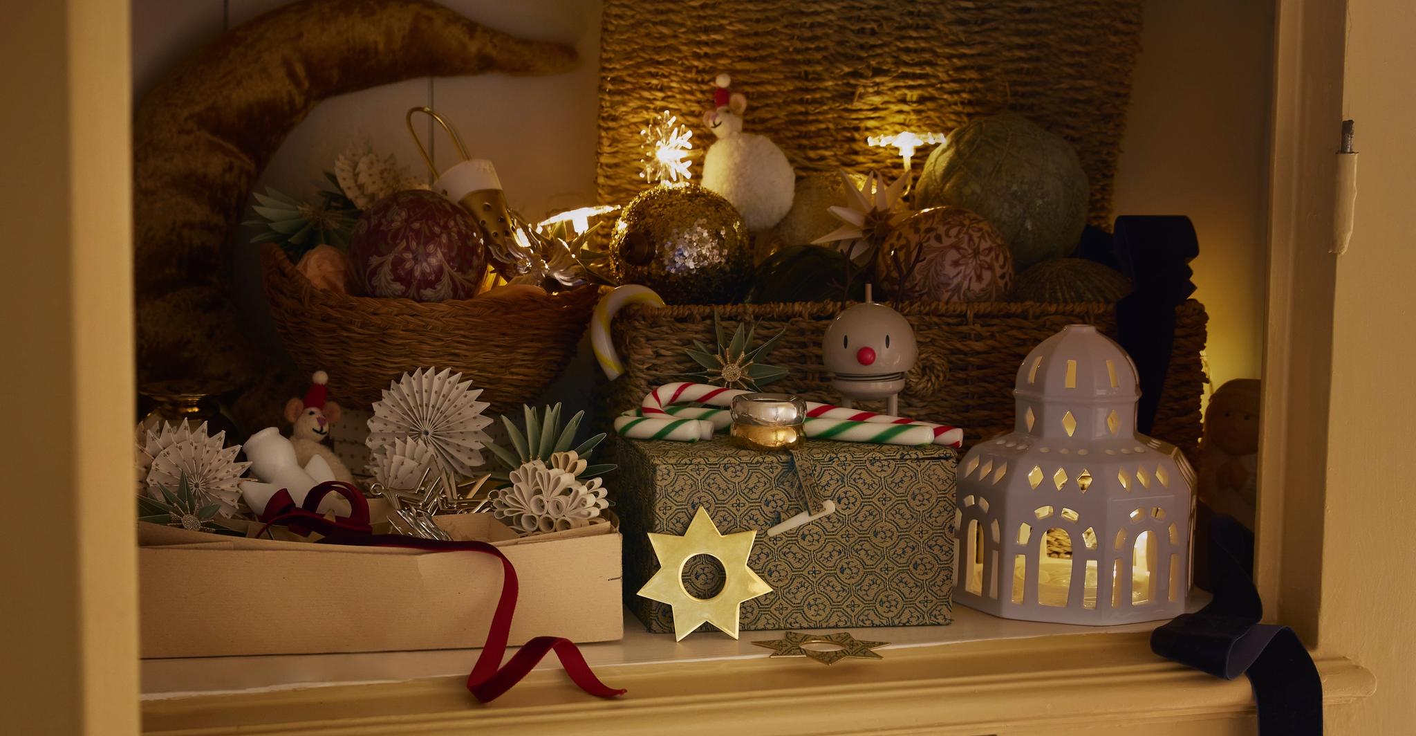 Ett festligt skåp fyllt med stjärnljus, ornament, presenter och tomtar arrangerade i korgar, vilket skapar en mysig juldekoration.