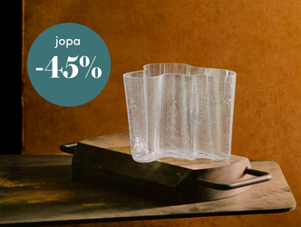 Kuva esittää Iittalan kirkasta Aalto-maljakkoa rustiikkisella alustalla, ja vasemmassa yläkulmassa on vihreä ympyrä, jossa lukee alennusteksti ”jopa -45 %”.