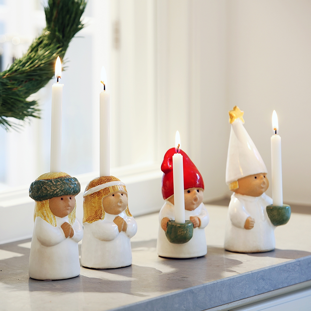 Four ceramic candle holders, two depicting children and two gnomes, each holding a lit white candle.