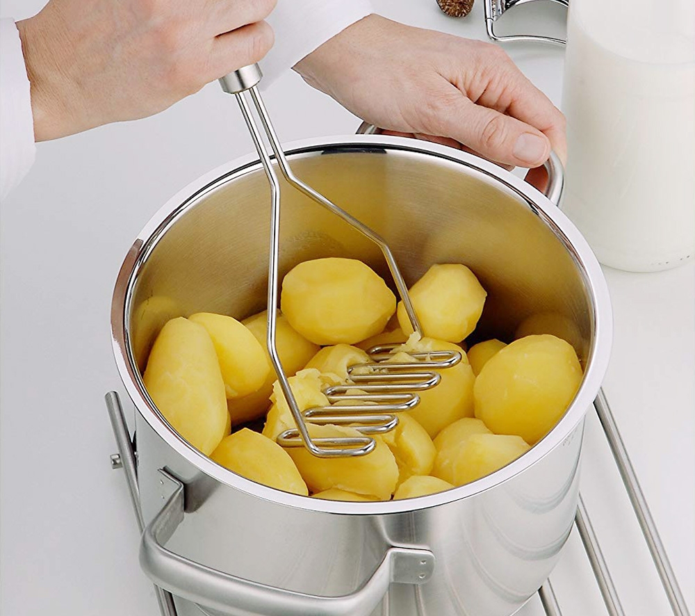En person använder en potatisstöt för att mosa kokta potatisar i en gryta.