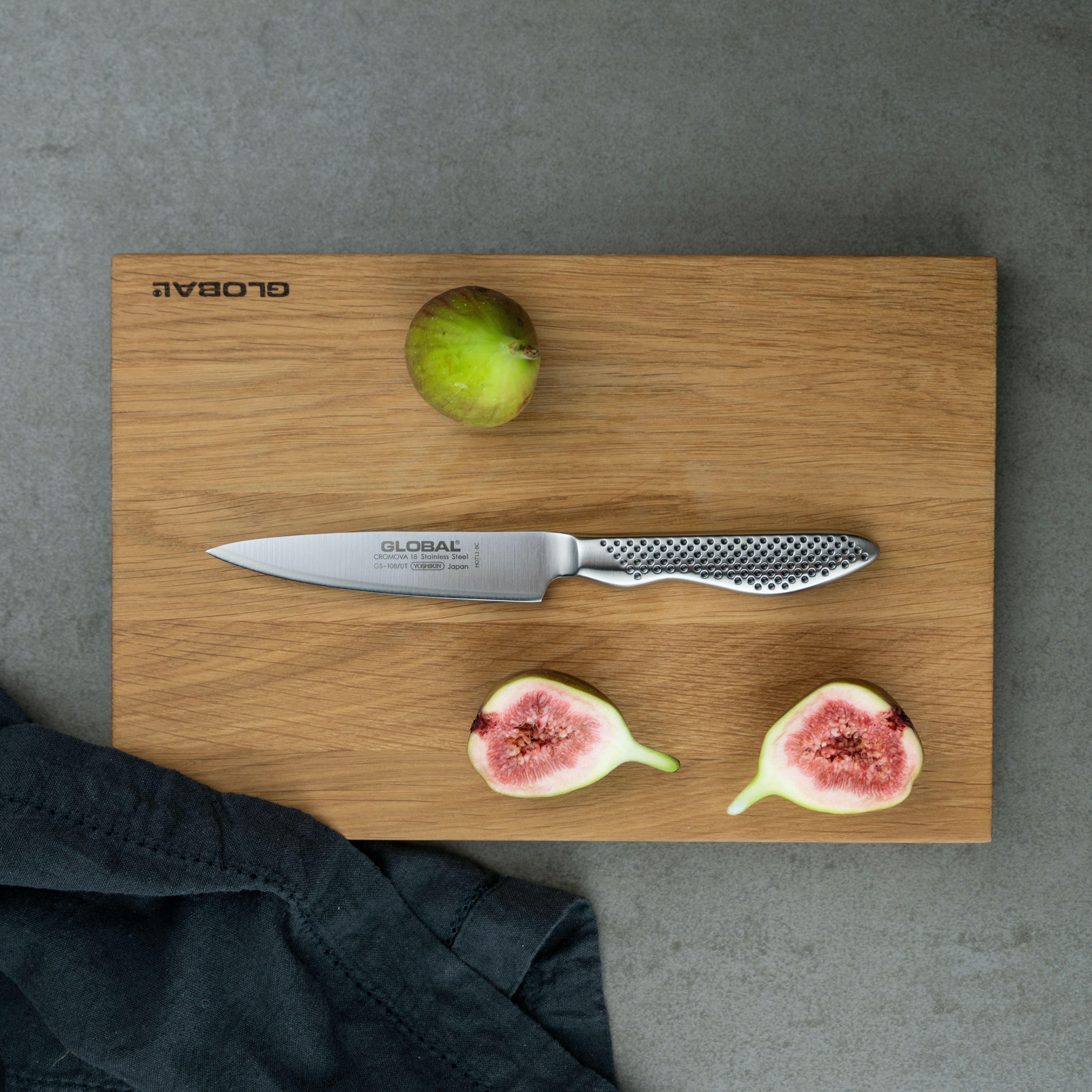 Global-kockkniv på träskärbräda med färska fikon, hel och delad, mot grå bänkskiva.