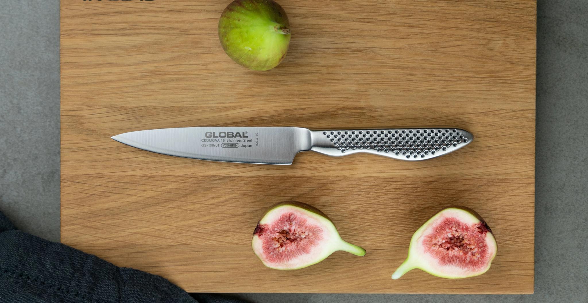 Global-kockkniv på träskärbräda med färska fikon, hel och delad, mot grå bänkskiva.