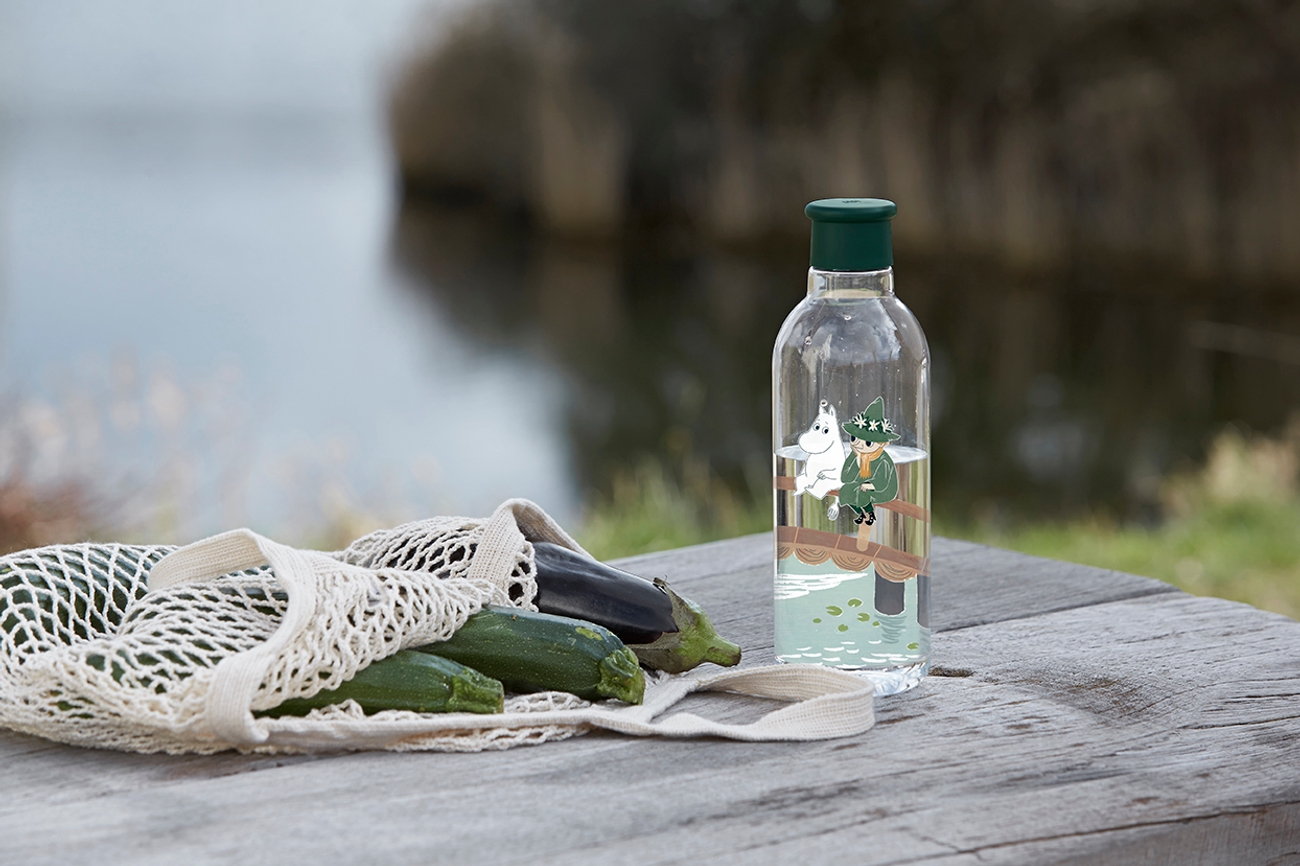 Vattenflaska med mumin på bänk vid en sjö