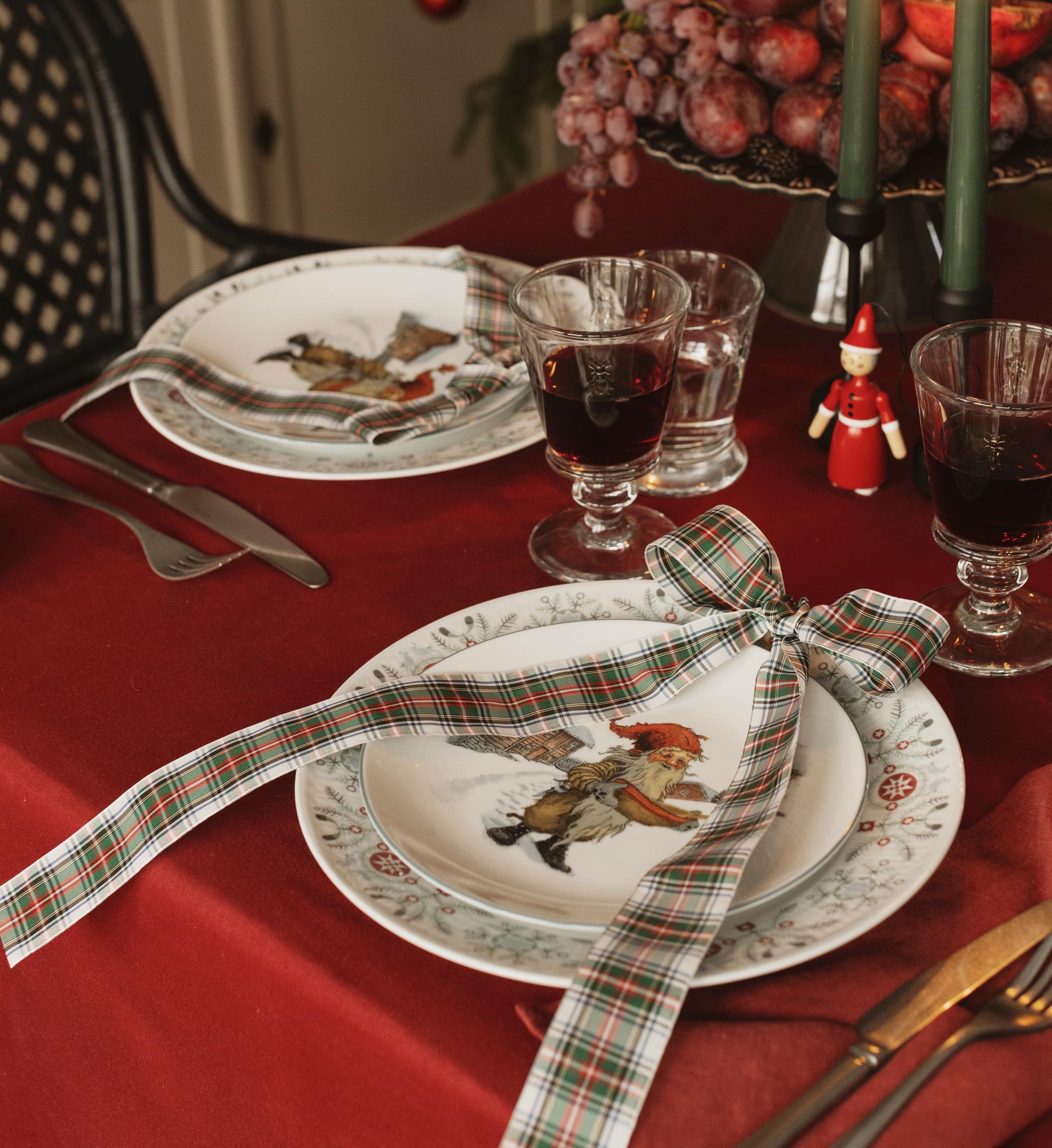 a christmas table setting with plates , wine glasses , candles and a christmas tree in the background .