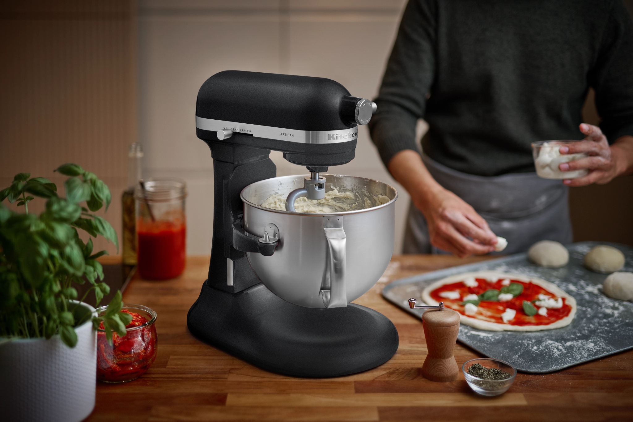 Musta KitchenAid-yleiskone taikinan teossa ja pizzan valmistusta puisella työtasolla