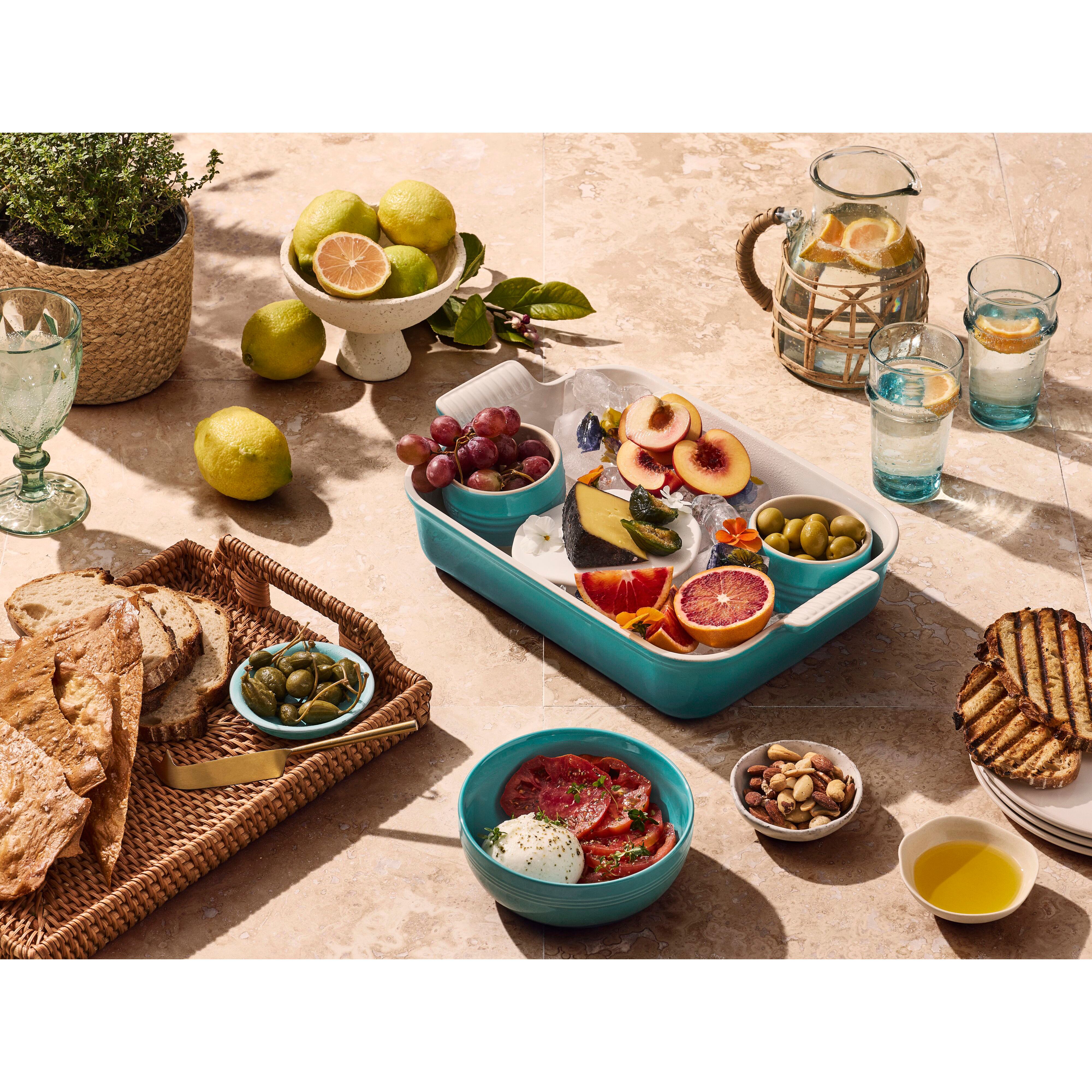 Ett dukat bord i solljus med medelhavsmat i blågröna skålar och ugnsformar.
