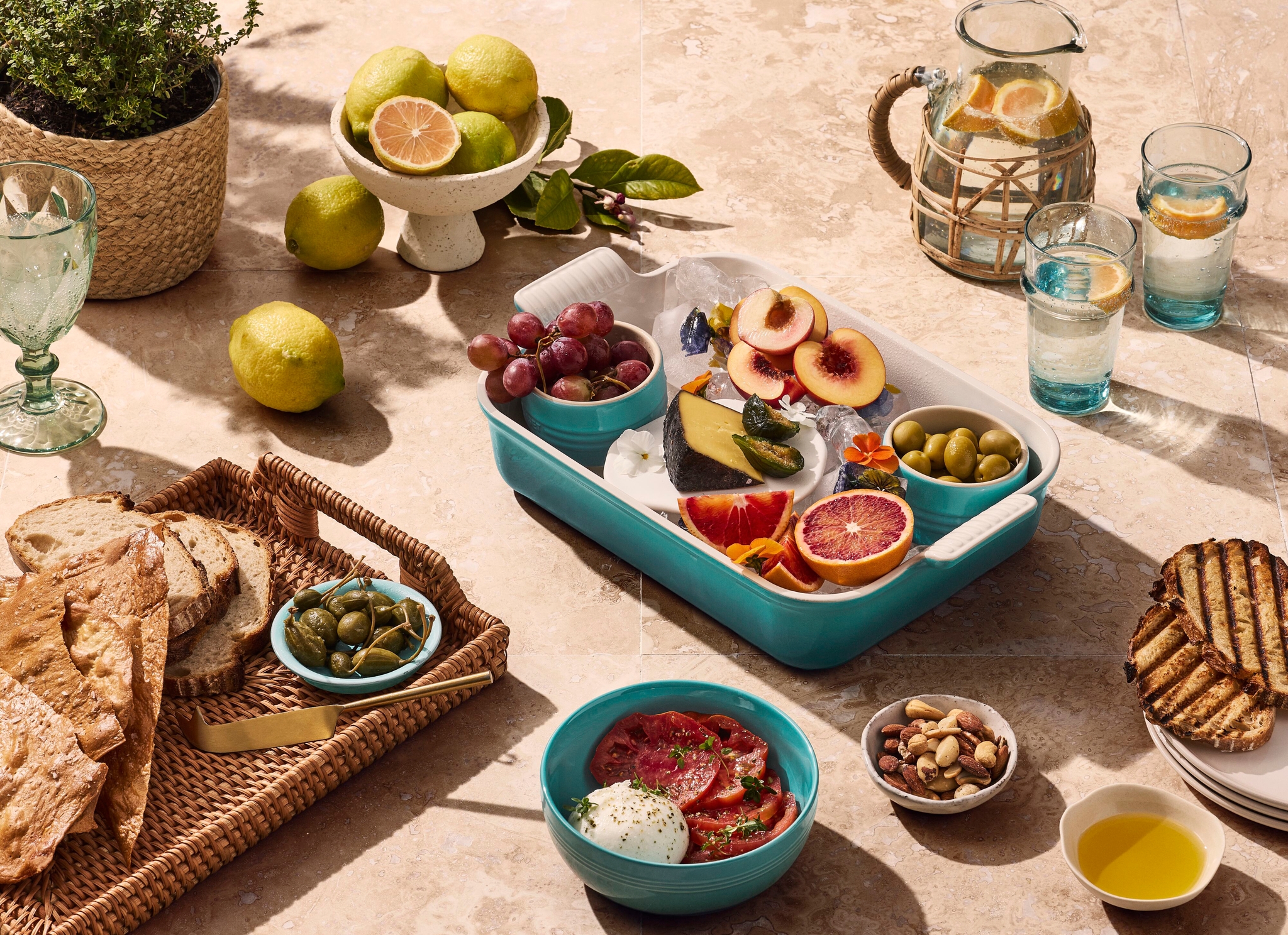 Ett dukat bord i solljus med medelhavsmat i blågröna skålar och ugnsformar.