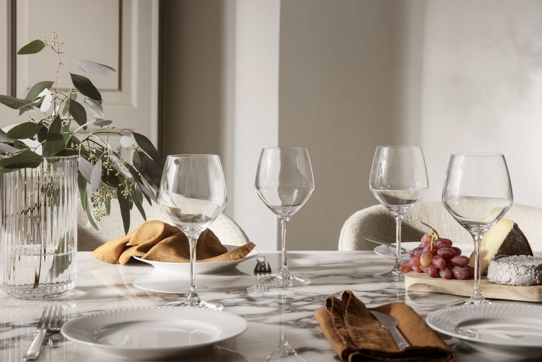 Elegant dukat marmorbord med vinglas, linneservetter, ost och vindruvor i mjukt dagsljus.