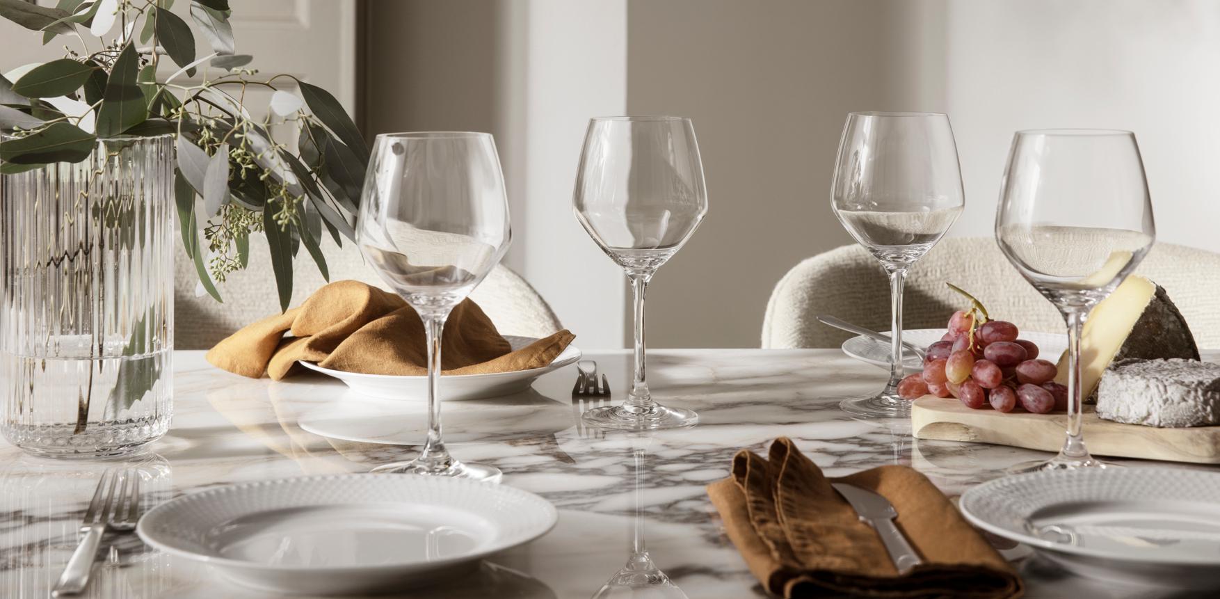 Elegant dukat marmorbord med vinglas, linneservetter, ost och vindruvor i mjukt dagsljus.