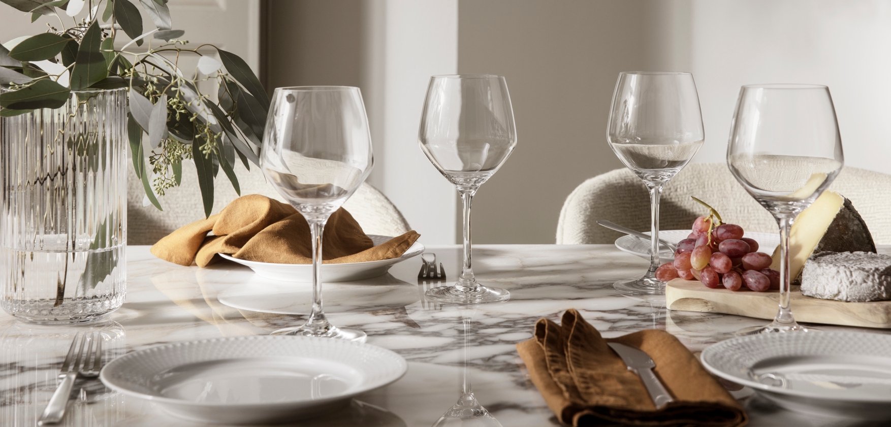 Elegant dukat marmorbord med vinglas, linneservetter, ost och vindruvor i mjukt naturligt ljus.