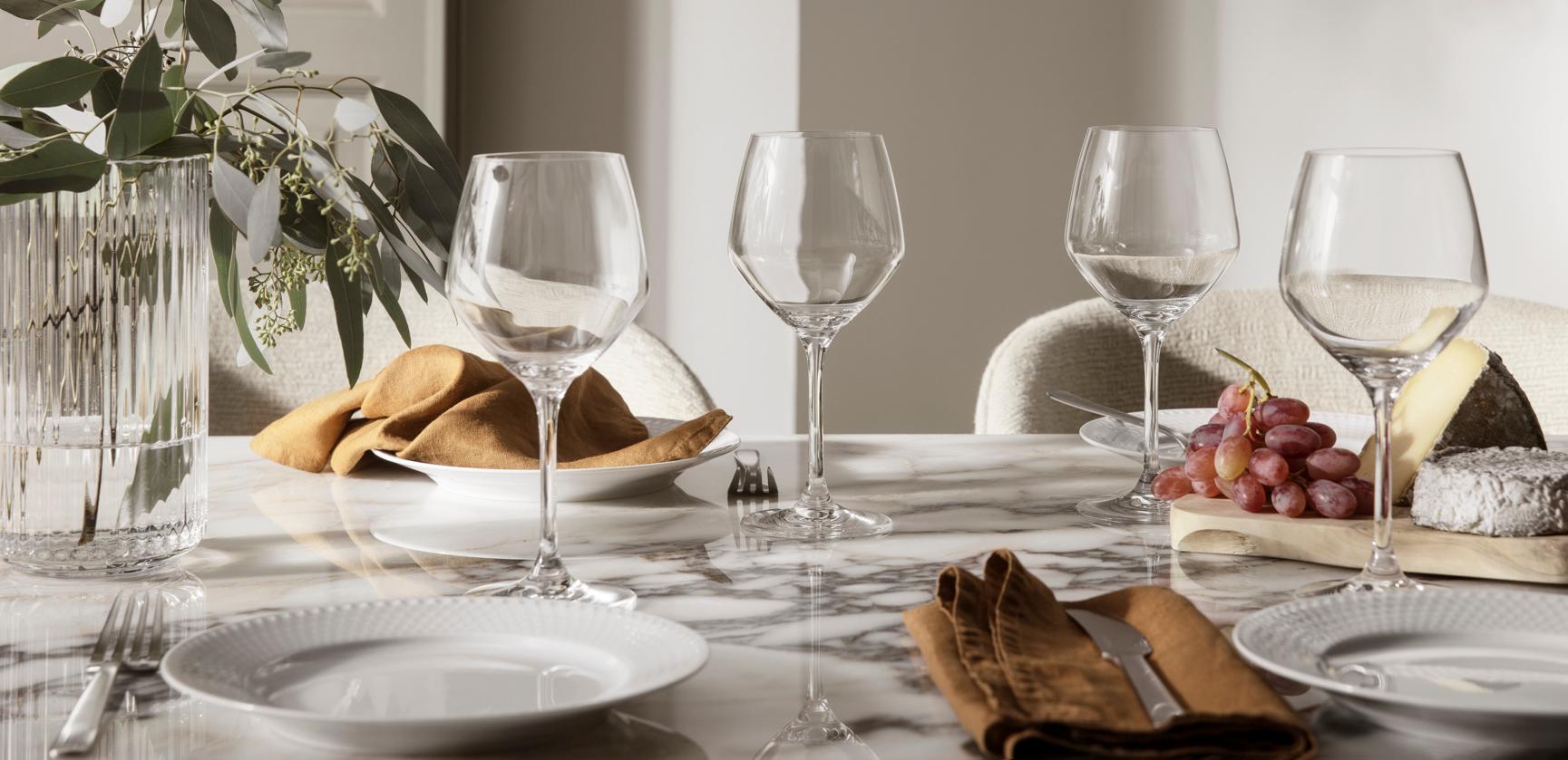 Elegant dukning på marmorbord med vinglas, eukalyptus, bröd, vindruvor och ostar.